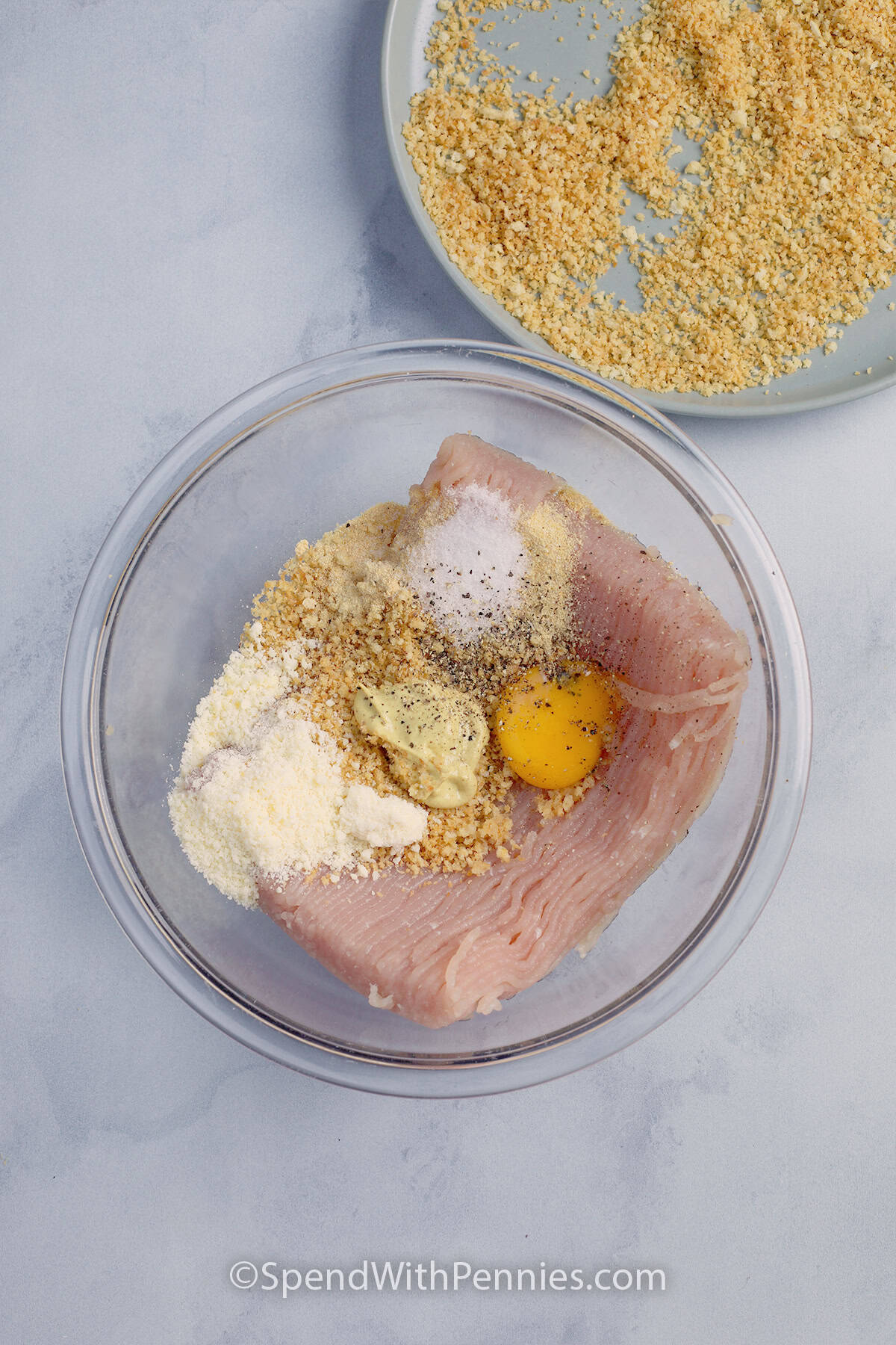 All ingredients to make a giant chicken cutlet in a bowl with toasted breadcrumbs off to the side.