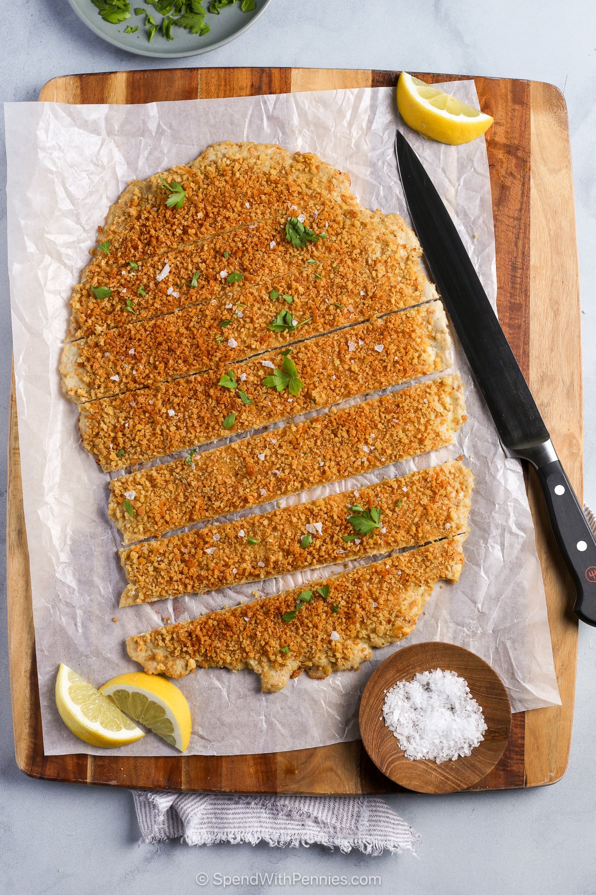 Sliced giant chicken cutlet on a cutting board with a knife.