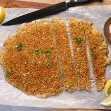 Sliced giant chicken cutlet on a cutting board with a knife and lemon slices