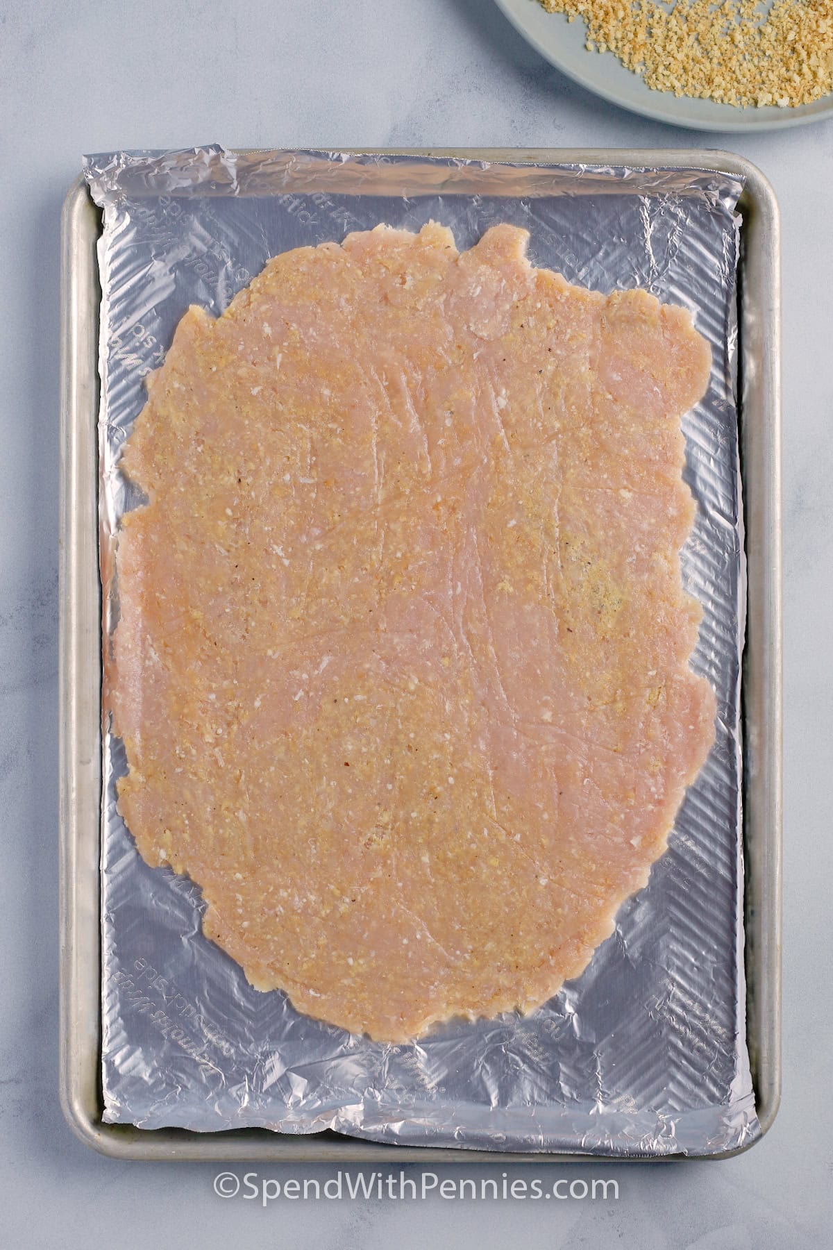 Raw chicken flattened on a baking sheet to make a giant chicken cutlet.