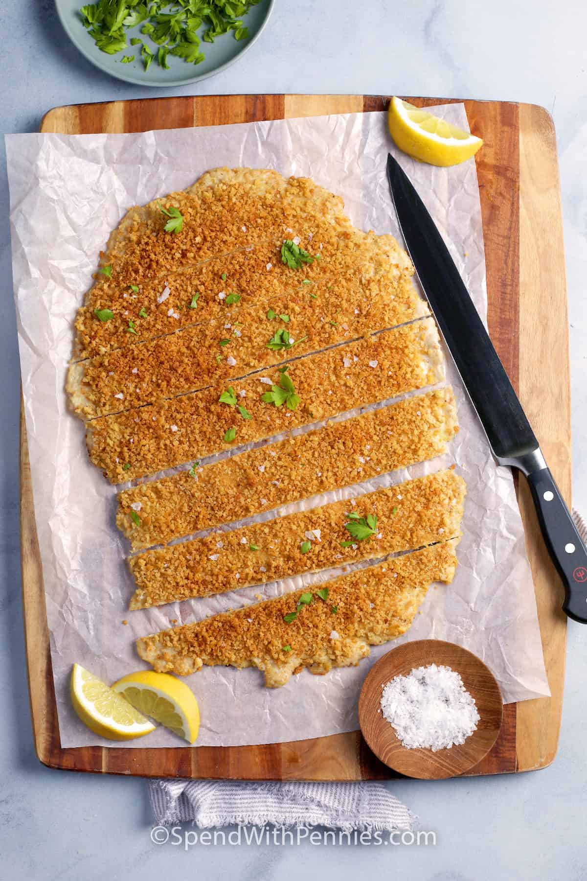 Sliced giant chicken cutlet on a cutting board with a knife.