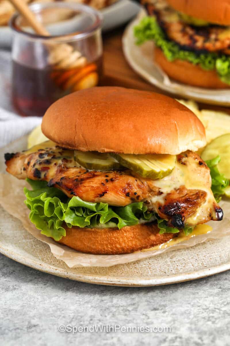 Hot Honey Chicken Sandwich on a plate with chips and hot honey in a jar in the background