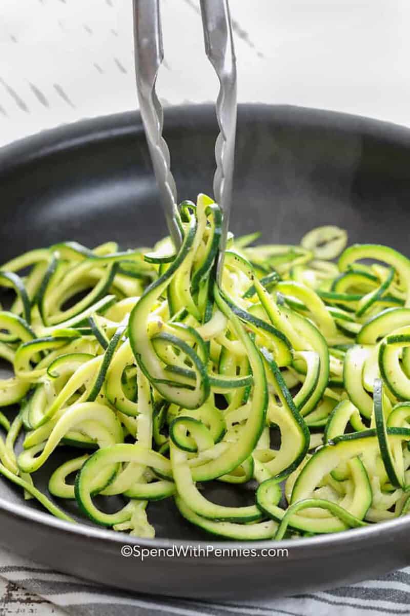 These spiralized zucchini noodles are fresh, lightly seasoned, and ready faster than traditional pasta. The recipe uses a medium spiralizer blade to create sturdy zoodles, then cooks them briefly in olive oil over medium-high heat. Butter is optional but gives the noodles a glossy finish and comforting flavor. Serve this versatile zucchini pasta as a low carb side, add a favorite sauce, or top it with chicken, shrimp, or meatballs. #spendwithpennies zucchini noodles in a pan with tongs