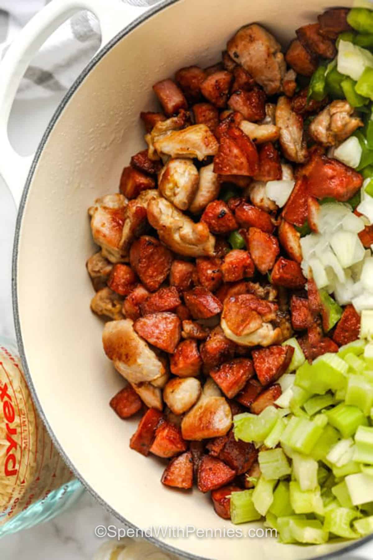 This shrimp Cajun jambalaya recipe is loaded with tender chicken, smoky sausage, Cajun seasoning, vegetables, and rice cooked right in the same pot. Adding the shrimp after baking keeps it juicy while the rice rests and finishes absorbing the broth. It is a flavorful, filling dinner that works for weeknights, Sunday supper, or leftovers. #spendwithpennies adding ingredients to pot to make Cajun Jambalaya