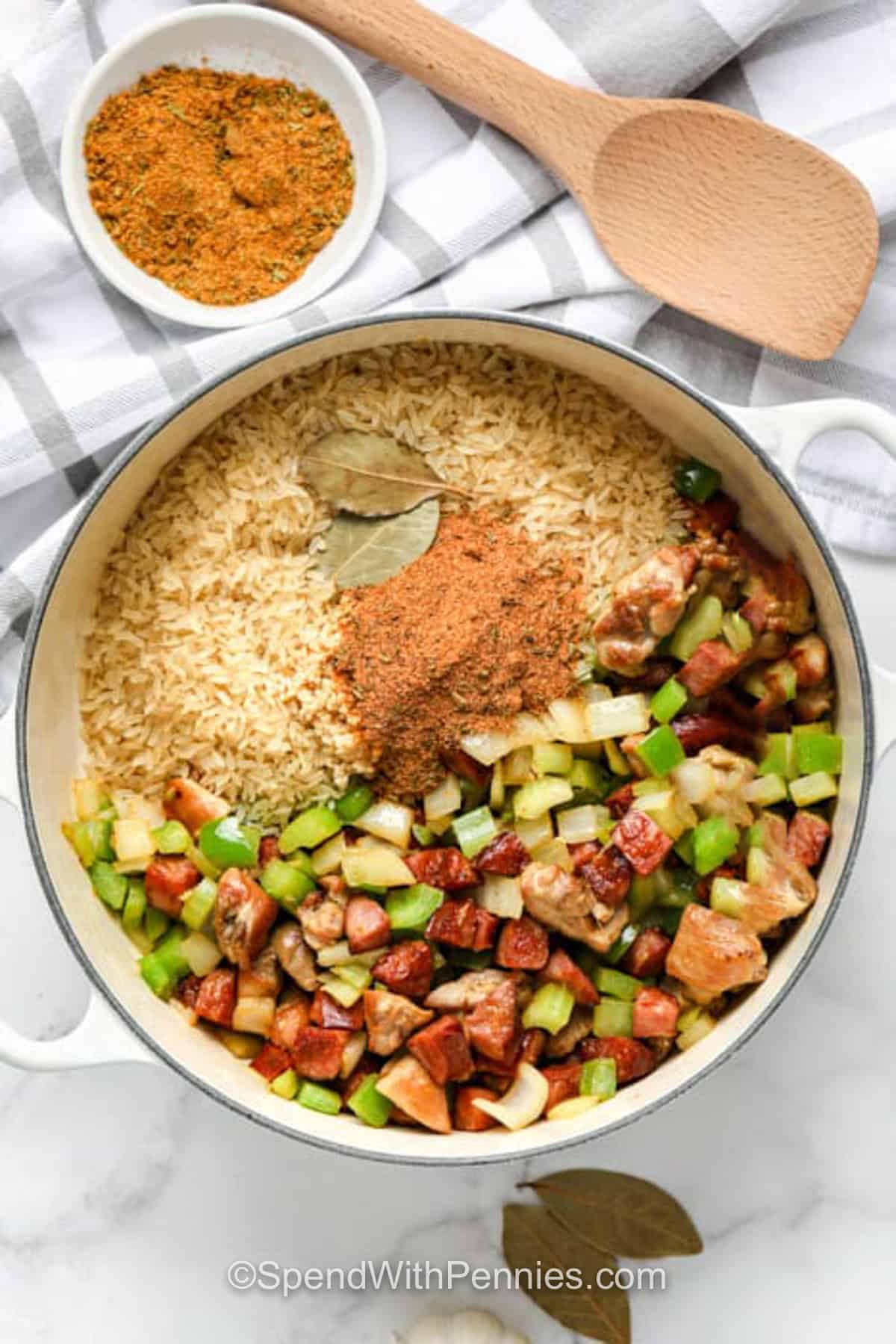 Cajun jambalaya is a comforting rice dinner made with andouille sausage, chicken, shrimp, bell pepper, celery, onion, and bold seasoning. The chicken and sausage are browned first to build flavor, then the rice bakes in broth until tender. It is a cozy family recipe that reheats well and can be made milder with smoked sausage. Save this recipe to your meal board. #spendwithpennies adding seasonings to Cajun Jambalaya ingredients