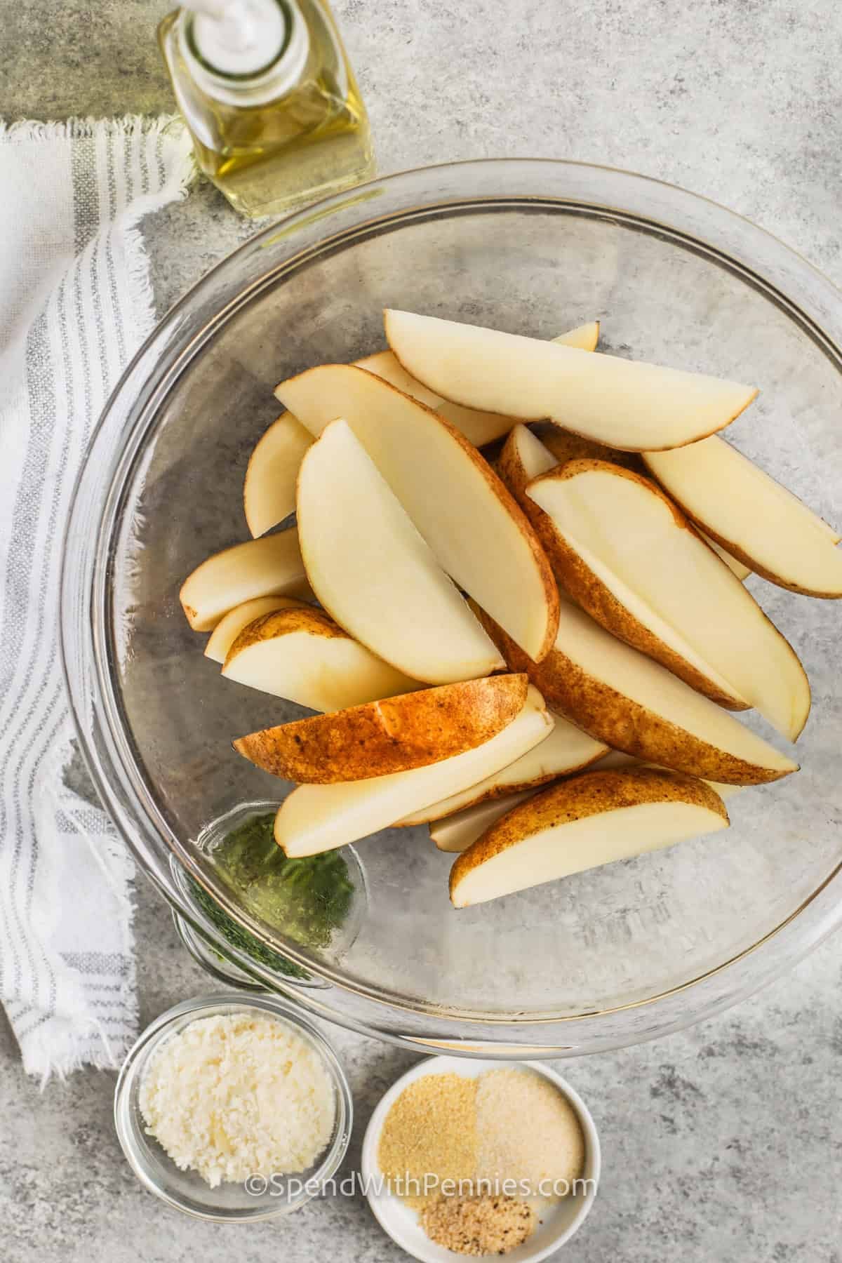 potato wedges in a bowl with seasoning in bowls around it to make Crispy Baked Potato Wedges