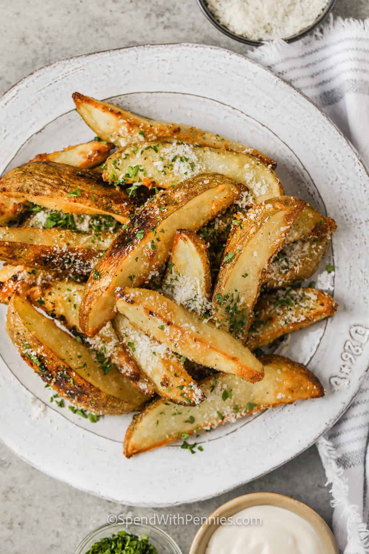 Seasoned potato wedges are an easy oven-baked alternative to traditional fries. Thick wedges of russet potato hold their shape while developing tender centers and browned edges, and the Parmesan seasoning adds salty, garlicky flavor. They work for casual dinners, game-day trays, or a hearty breakfast plate. Save this seasoned potato wedges recipe and serve it with your favorite dipping sauce. #spendwithpennies plate of Crispy Baked Potato Wedges