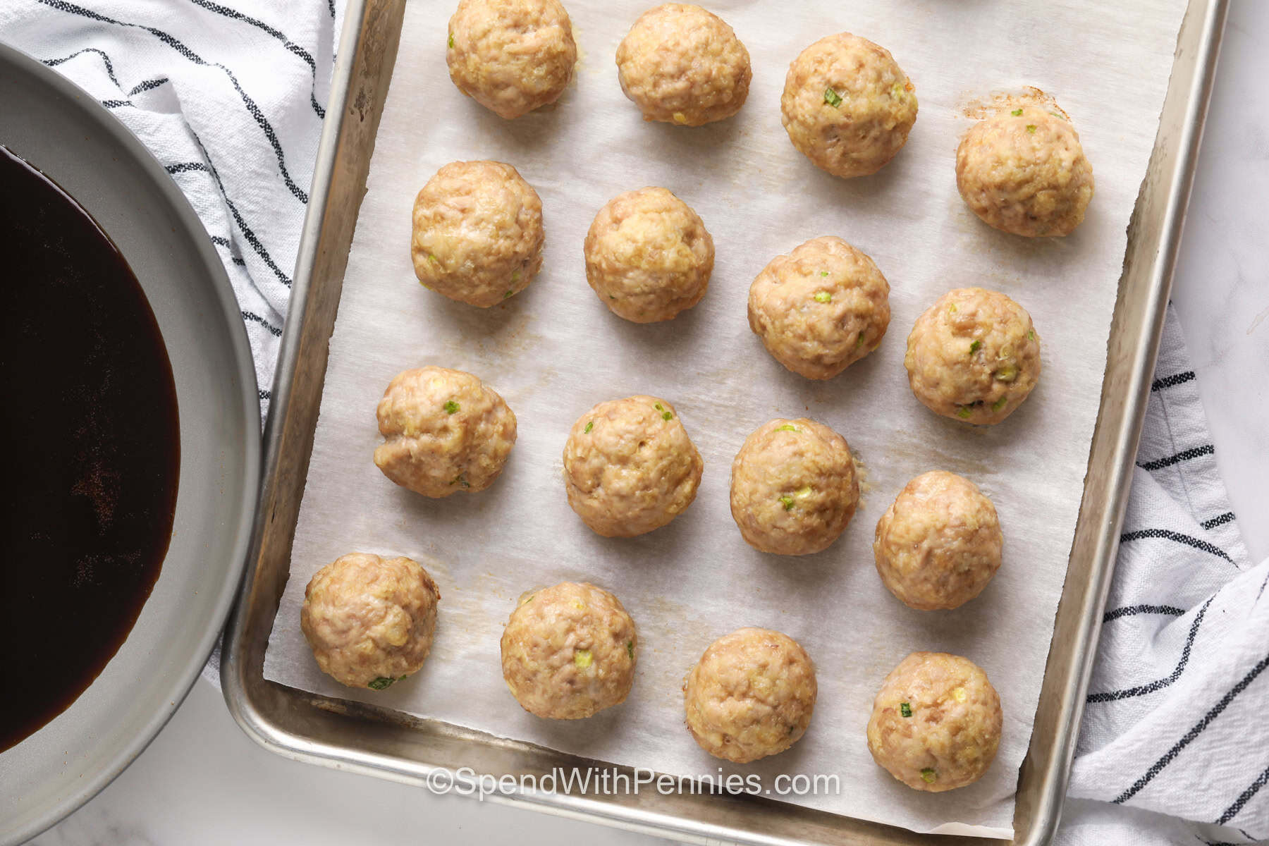 Hoisin meatballs with ginger and green onions are ready in just over 30 minutes and can be served so many ways. Bake the pork meatballs until tender, simmer the sweet and savory hoisin sauce, and toss everything together for a cozy, saucy recipe that is freezer-friendly and great for leftovers. #spendwithpennies uncooked hoisin meatballs on a pan