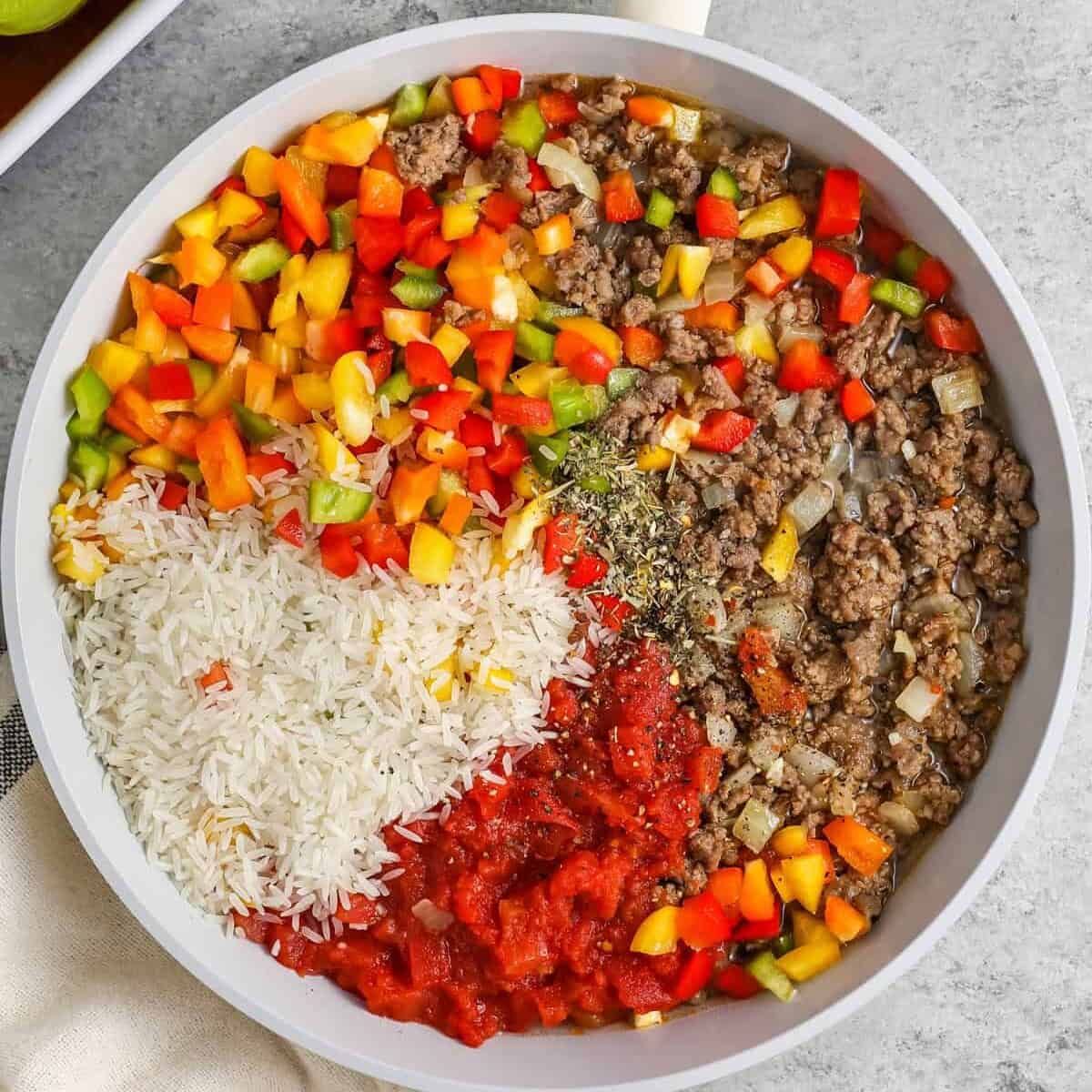These stuffed bell peppers are cozy, saucy, and packed with a hearty beef and rice filling. Italian sausage adds extra flavor, while marinara sauce keeps the peppers moist as they bake. Use red, yellow, orange, or green bell peppers depending on what you have. Top with mozzarella or cheddar cheese for a melty finish that makes this dinner feel extra comforting. #spendwithpennies ingredients in a pan to make Stuffed Peppers filling
