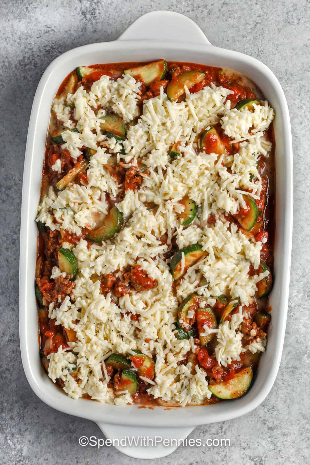 adding cheese on top of Zucchini Hamburger Casserole in the dish before cooking