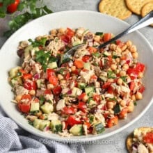 Mediterranean Tuna Salad in a bowl with a spoon and some on crackers beside it