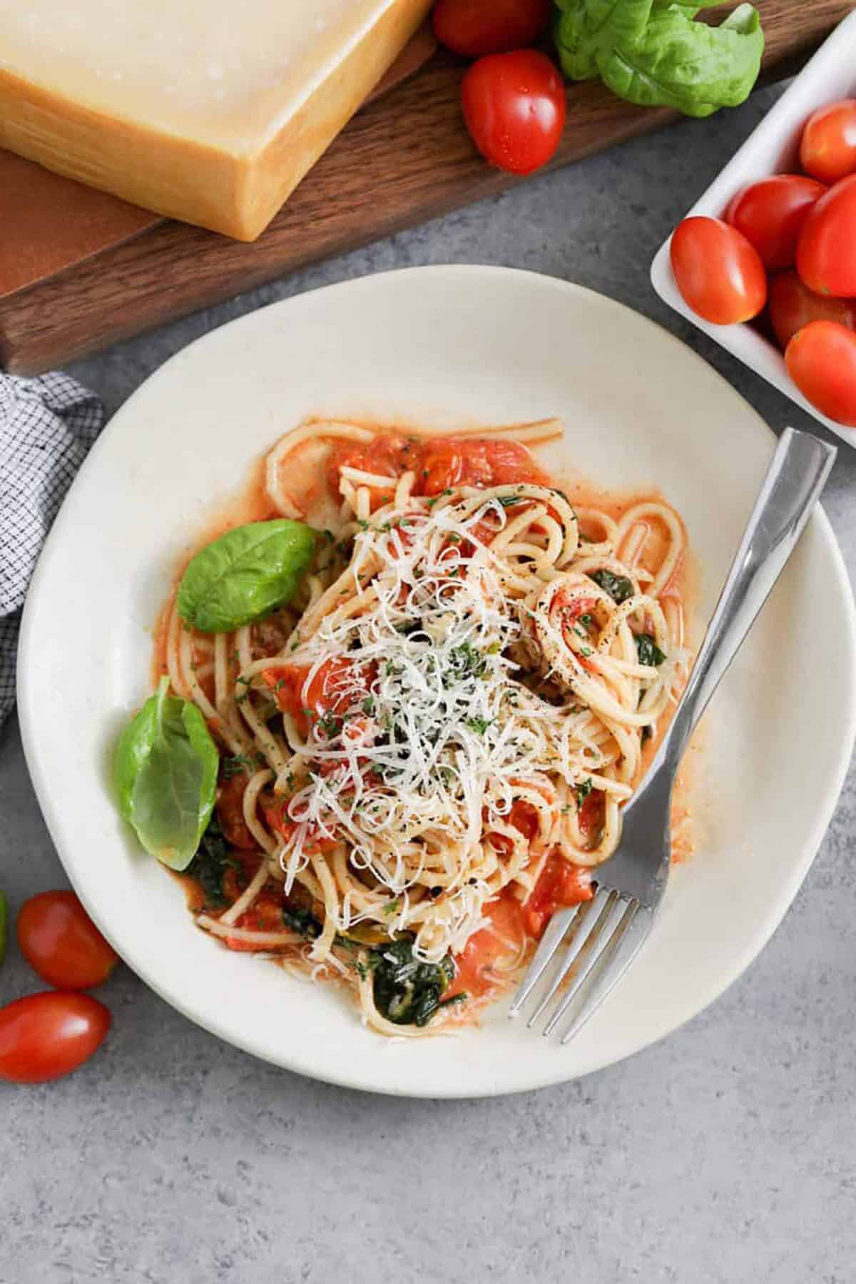 This easy one-pot spaghetti recipe is light, fresh, and surprisingly simple to make in just one pot. Juicy cherry tomatoes, garlic, lemon zest, basil, and spinach give the pasta plenty of color and flavor, while freshly grated Parmesan melts into the starchy sauce. There is no separate pasta pot and no draining, which makes cleanup especially easy after dinner. Save this easy spaghetti recipe when you need a quick, meatless weeknight meal. #spendwithpennies plate of One Pot Spaghetti with cheese on top
