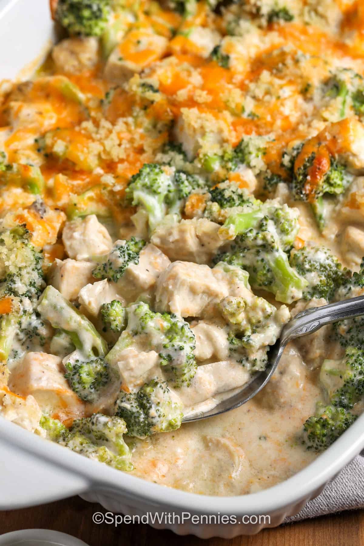 This chicken divan recipe combines tender chicken, fresh broccoli, sharp cheddar, and a creamy seasoned sauce in one comforting casserole. Panko breadcrumbs mixed with melted butter create a golden topping that adds just the right amount of crunch. Use rotisserie chicken to keep prep especially quick, then serve this creamy chicken casserole over rice, noodles, or mashed potatoes. Save the recipe for an easy weeknight dinner. #spendwithpennies dish of Chicken Divan with a spoon.