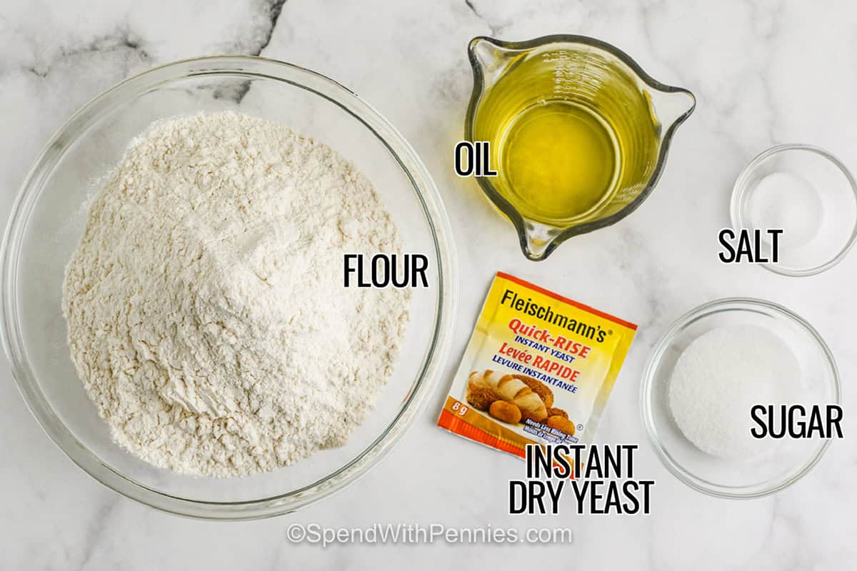 bowls of flour , salt and sugar with measuring cup of oil and instant dry yeast package with labels to make Homemade Pizza Dough