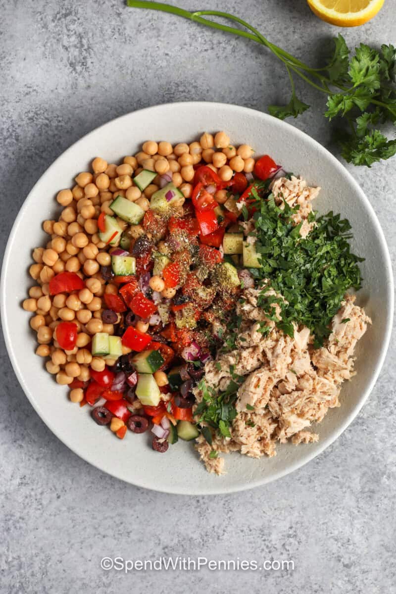 Canned tuna, mixed chopped veggies, and chickpeas in a bowl topped with herbs and seasonings.