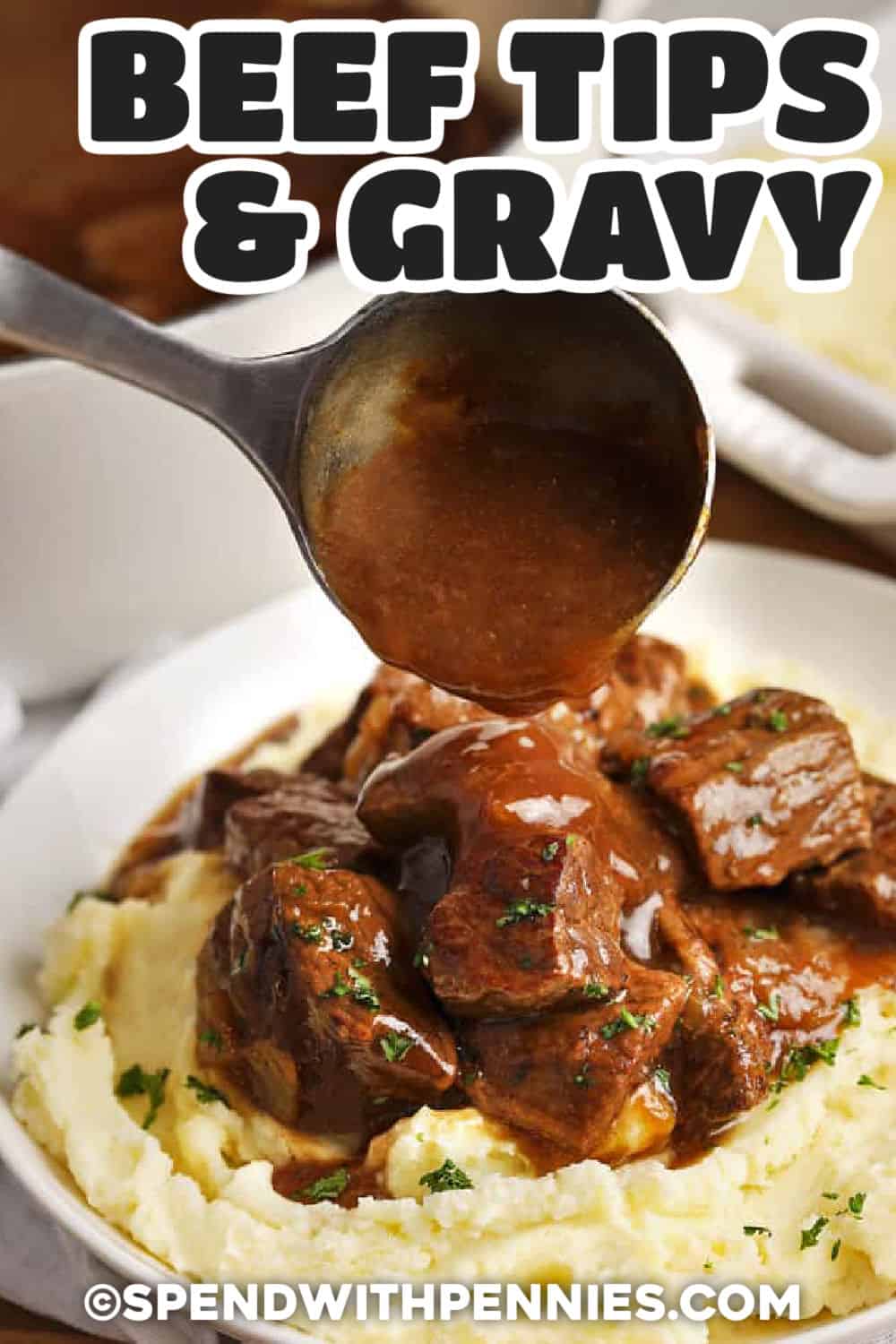 Easy beef tips and gravy combine browned chuck roast with a savory onion gravy for a satisfying stovetop dinner. The beef cooks gently until tender, so an economical cut becomes rich and flavorful without complicated prep. Spoon the beef and plenty of gravy over mashed potatoes and add a simple vegetable for a complete meal. This recipe is also great for make-ahead dinners and leftovers. Save it for an easy family comfort food dinner. #spendwithpennies adding gravy to Beef Tips on mashed potatoes and a title