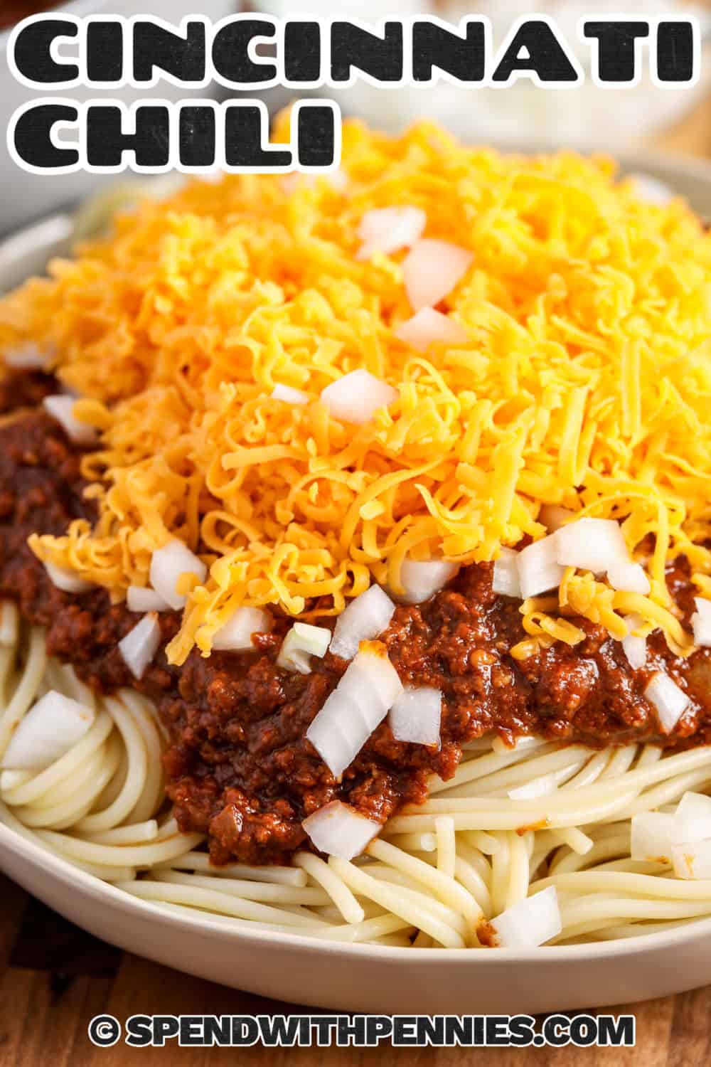 Cincinnati chili is the cozy ground beef dinner to make when traditional chili is not quite what you are craving. The stovetop sauce combines tomato, chili powder, cocoa, cinnamon, and allspice, then slowly simmers until flavorful and spoonable. Serve it over hot spaghetti with plenty of cheddar, plus chopped onion or beans for a classic 4-way or 5-way plate. Save this Cincinnati style chili for an easy weekend dinner. #spendwithpennies Cincinnati Chili on spaghetti with cheese and a title.