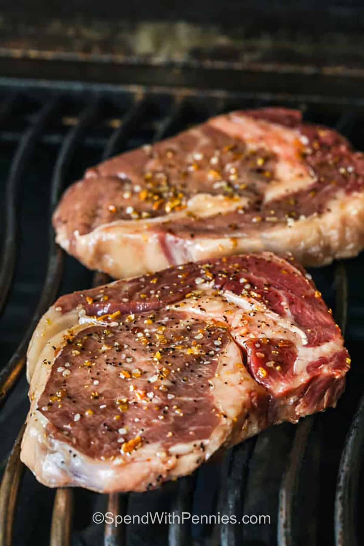 steaks on the grill with seasoning to make Perfect Ribeye Steak