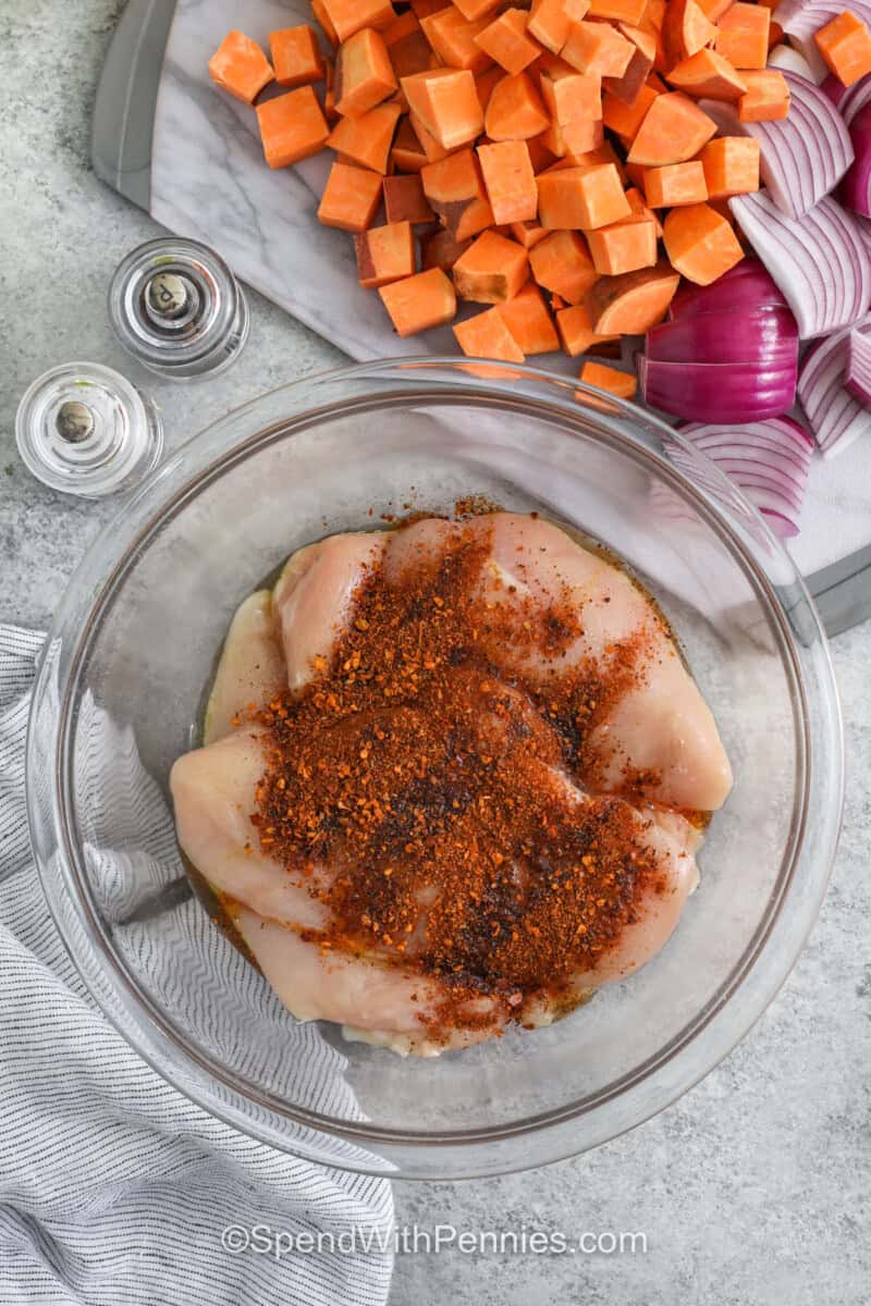 adding seasoning to chicken to make Sheet Pan Chicken and Sweet Potatoes