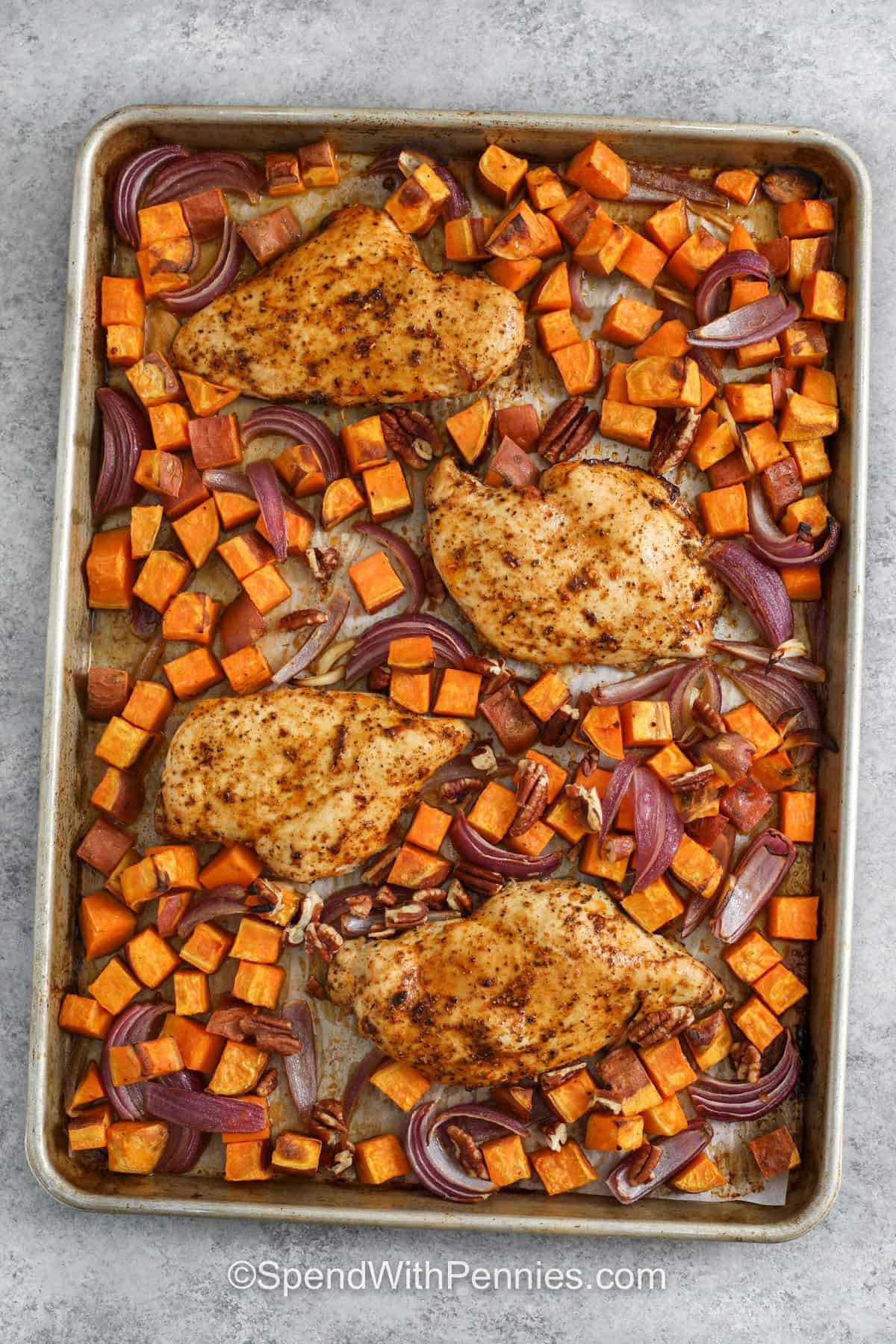 Make sheet pan chicken and sweet potatoes when dinner needs to be simple without sacrificing flavor. Cajun-seasoned chicken breasts roast alongside honey-coated sweet potatoes, garlic, and red onion, creating a delicious mix of savory spice and natural sweetness. Pecans can be added near the end for extra toasted crunch or skipped entirely. Add this easy sheet pan chicken dinner to your weeknight recipe collection. #spendwithpennies top view of Sheet Pan Chicken and Sweet Potatoes