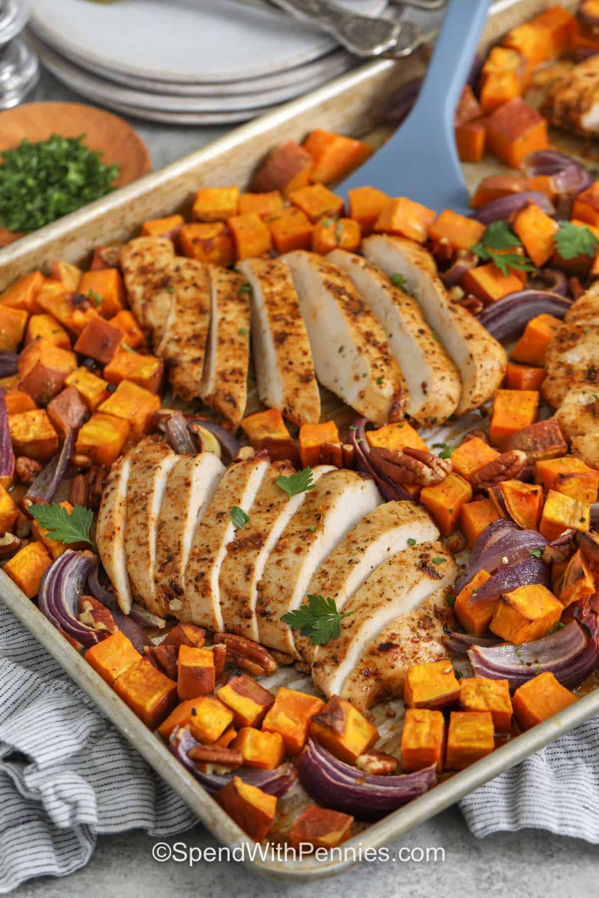 This sheet pan chicken and sweet potatoes recipe combines juicy chicken breast with caramelized sweet potatoes and red onion for an easy, satisfying dinner. Cajun seasoning brings warm, savory flavor while honey balances the spices and encourages golden roasted edges. Optional pecans add a welcome bit of crunch at the end. Keep this flavorful chicken sweet potato sheet pan dinner handy for your next weeknight meal. #spendwithpennies Sheet Pan Chicken and Sweet Potatoes on the sheet pan with a spatula