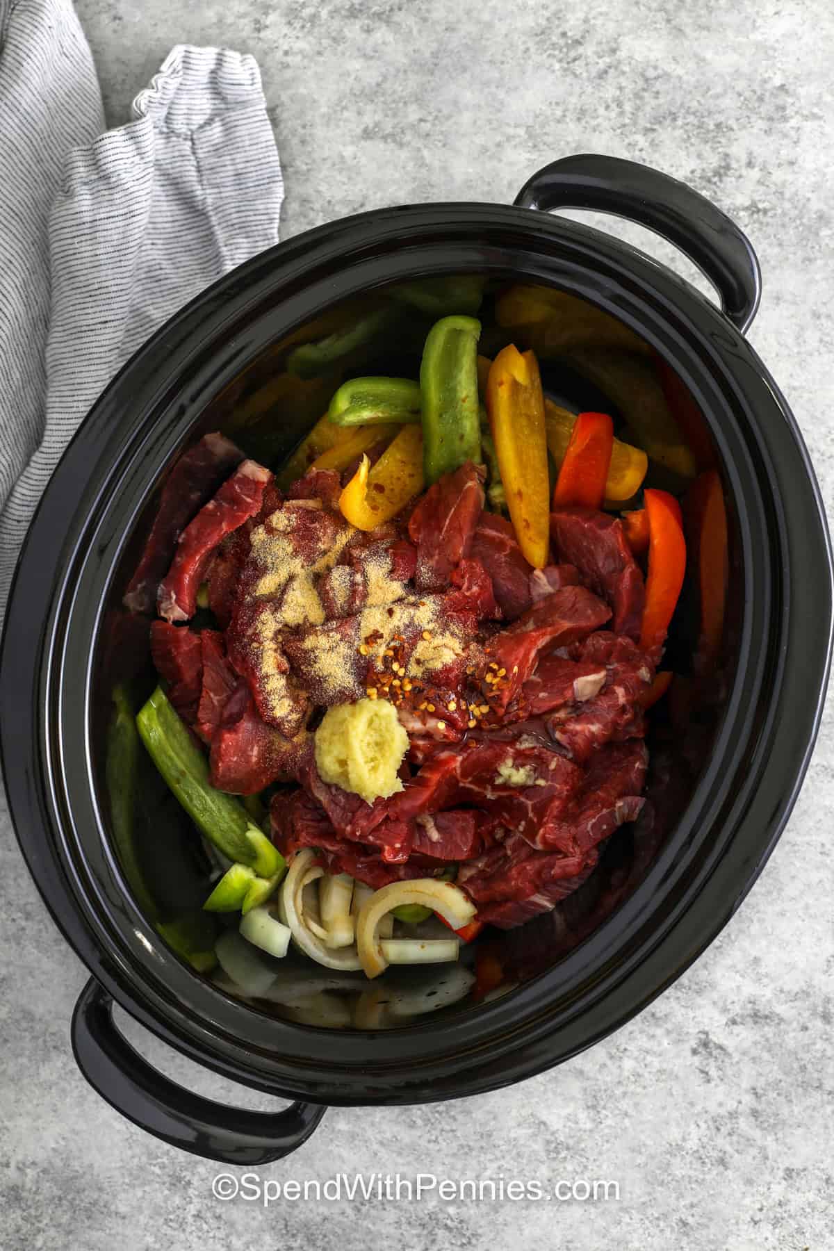 Slow cooker pepper steak brings tender beef, sweet bell peppers, and onions together in a rich and savory sauce. Soy sauce, fresh ginger, honey, and garlic create a wonderful balance of sweet and savory flavors. A touch of red pepper flakes adds just enough spice to keep things interesting. Spoon the tender beef and vegetables over rice or noodles for an easy dinner. Try this family-friendly recipe the next time you need a tasty meal. #spendwithpennies adding ingredients to pot to make Slow Cooker Pepper Steak.
