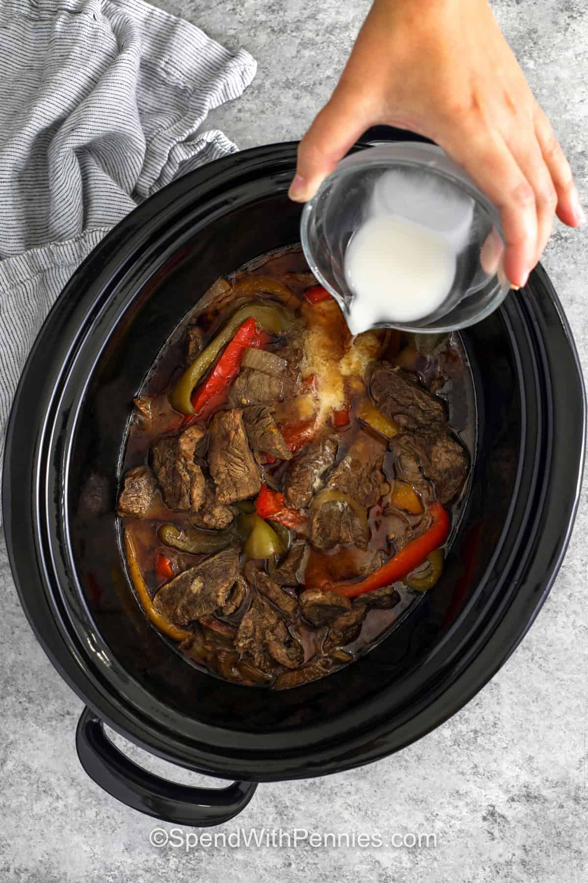 Slow cooker pepper steak turns simple ingredients into a flavorful dinner everyone can enjoy. Tender strips of beef cook with bell peppers and onions in a savory sauce made with soy sauce, ginger, honey, and Worcestershire sauce. Red pepper flakes add a little heat, while rice or noodles make it a filling meal. This easy beef recipe is perfect for busy weeknights when you want something comforting. Save this recipe and make it soon. #spendwithpennies adding cornstarch mixture to ingredients to make Slow Cooker Pepper Steak.