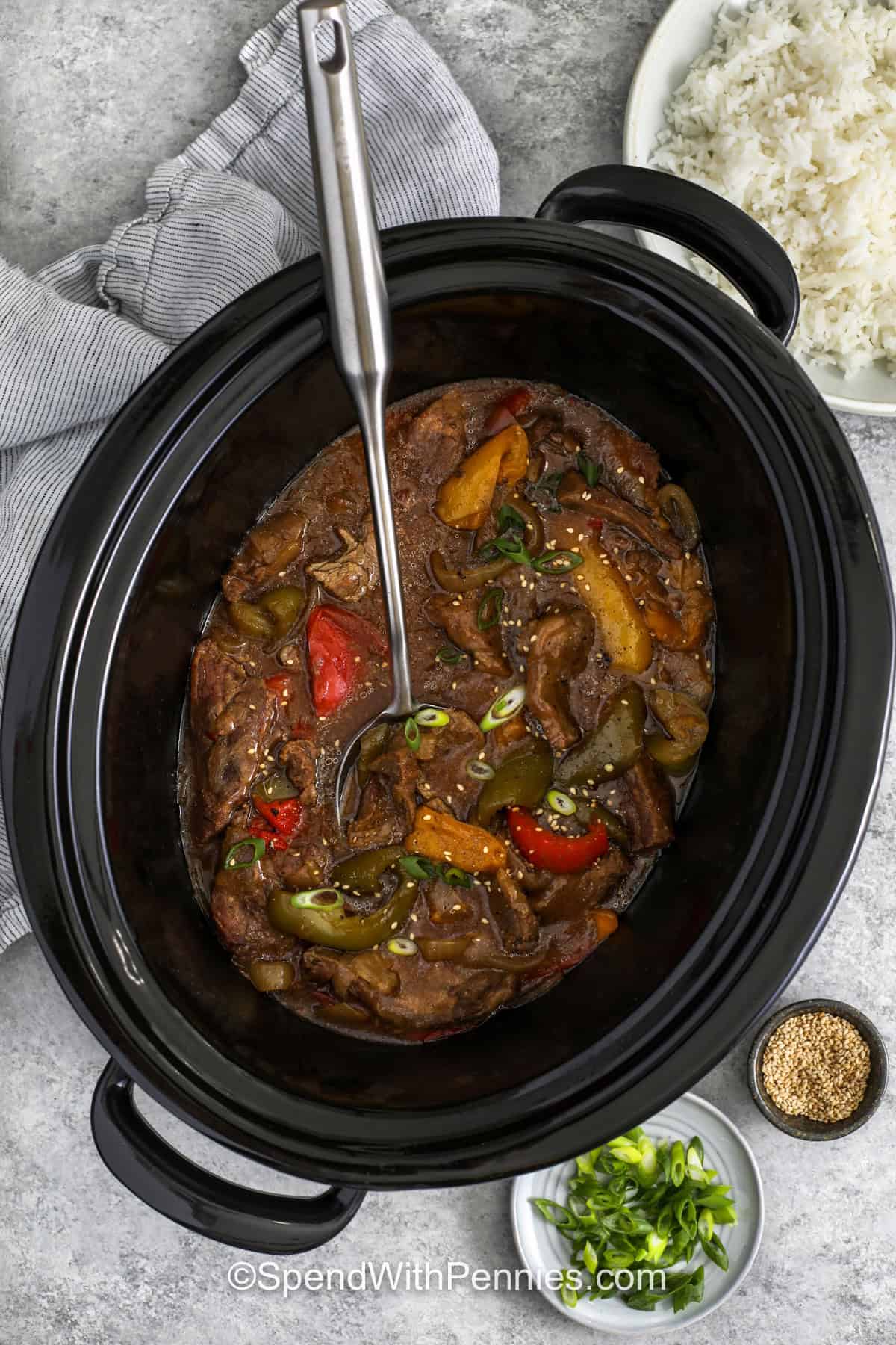 Slow cooker pepper steak is an easy family dinner made with tender beef, colorful bell peppers, and onions. The savory-sweet sauce combines soy sauce, ginger, honey, Worcestershire sauce, and garlic for delicious flavor in every bite. Serve the saucy beef and vegetables over rice or noodles for a hearty meal. Green onions and sesame seeds add a tasty finishing touch. Add this simple slow cooker dinner to your menu and give it a try. #spendwithpennies Slow Cooker Pepper Steak in the slow cooker.