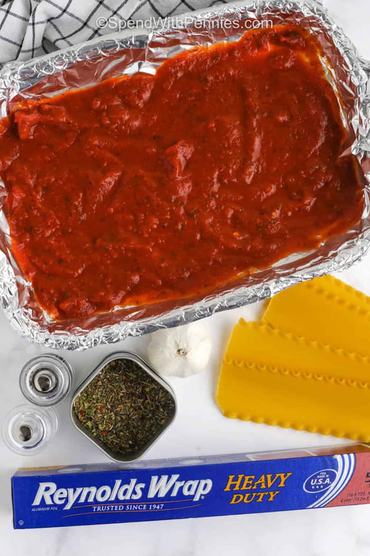 spinach lasagna preparation in foil lined casserole dish, with noodles and seasoning on the side.