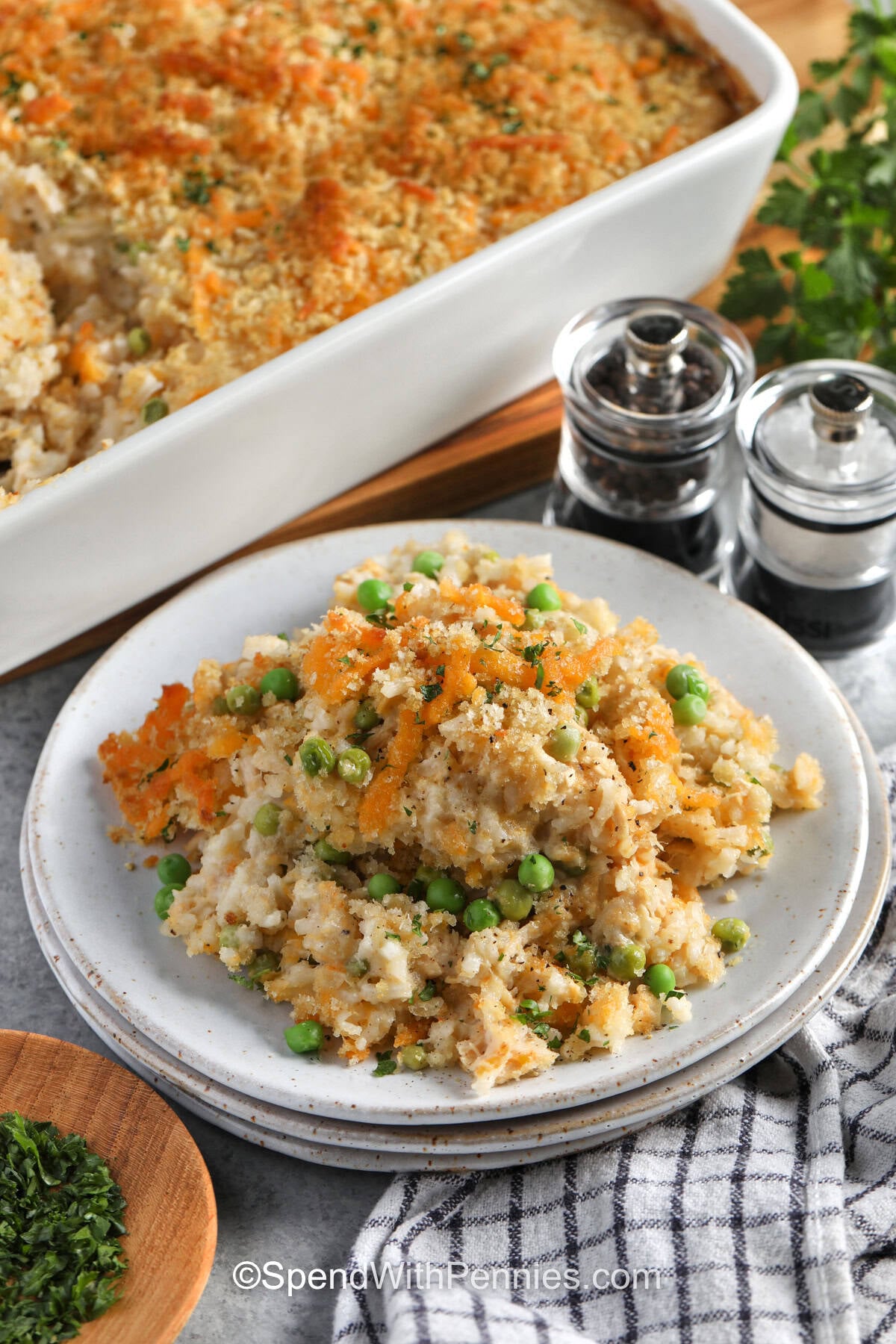This cheesy tuna rice casserole combines flaky canned tuna, tender instant rice, peas, Alfredo sauce, and sharp cheddar in one comforting bake. Covering the casserole first gives the rice time to absorb the creamy sauce, while a final layer of buttery Panko bakes until crisp and golden. It is hearty, practical, and made with ingredients that are easy to keep on hand. Pin this recipe for your next cozy dinner. #spendwithpennies plated casserole dish of Tuna Rice Casserole with casserole dish full.