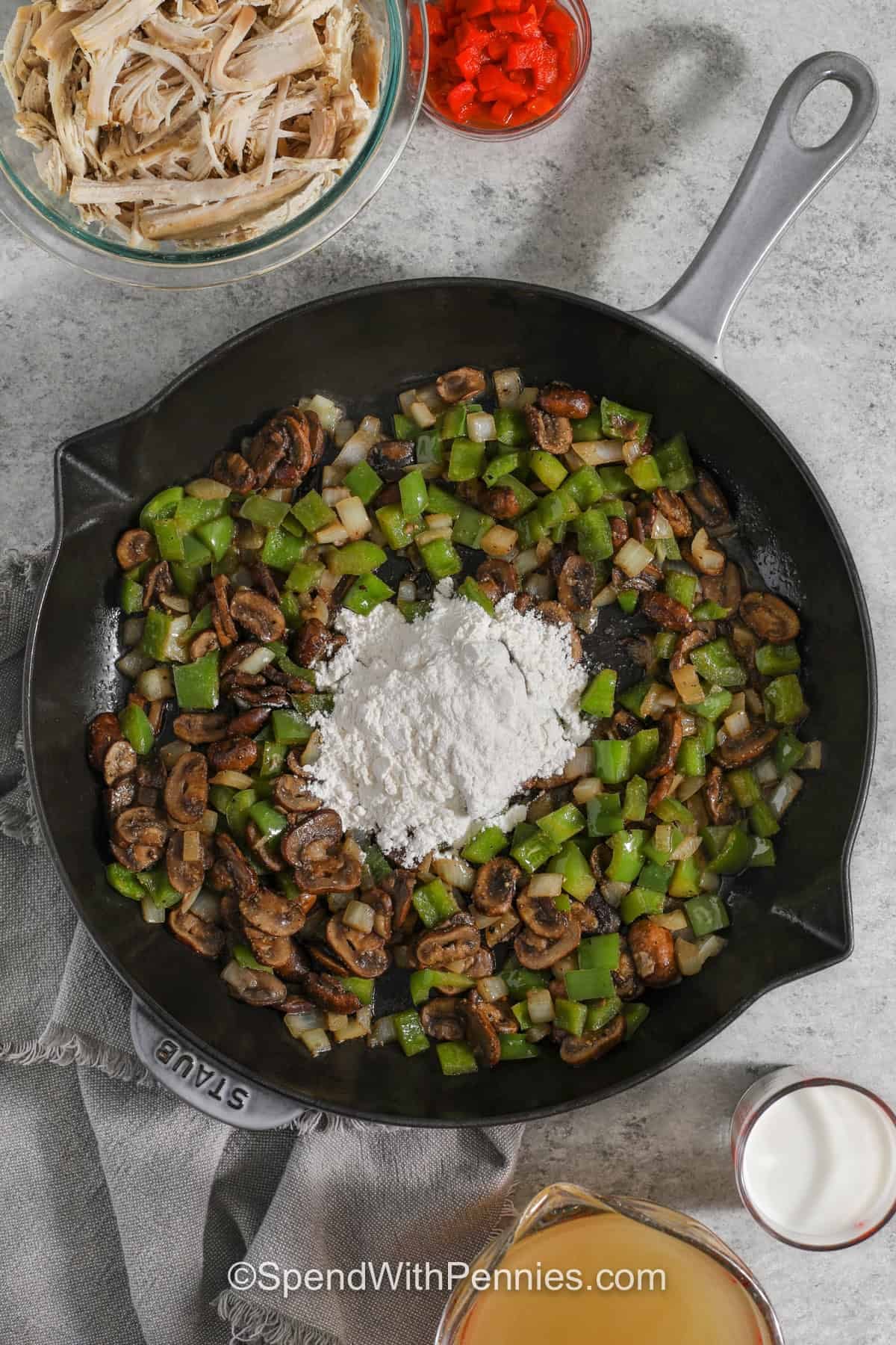 Turkey a la king is classic comfort food made with simple, everyday ingredients. Tender turkey, mushrooms, onions, peppers, peas, and pimentos come together in a creamy sauce that is full of flavor. Serve this hearty turkey dinner over rice, pasta, or biscuits for an easy meal the whole family can enjoy. Everything cooks in one skillet, so cleanup is simple too. Try this cozy recipe for dinner tonight. #spendwithpennies adding flour to mushroom onion and pepper mix in pan to make Turkey A La King