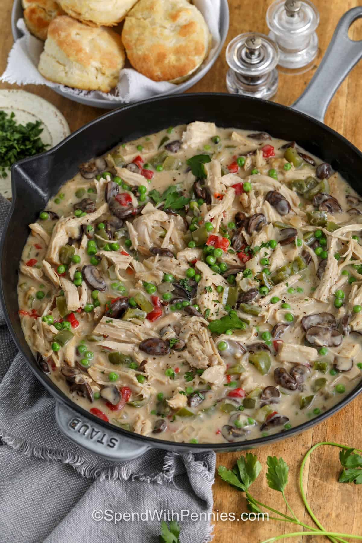 Turkey à la king is a delicious choice when you want a warm and comforting turkey dinner. This easy recipe combines cooked turkey with mushrooms, onions, bell pepper, peas, and pimentos in a creamy homemade sauce. Spoon it over rice, pasta, or biscuits for a hearty family meal that makes great use of leftovers. With simple ingredients and one skillet, this recipe is easy to add to your regular dinner rotation. Make it tonight. #spendwithpennies Turkey A La King in the pan with a bowl of biscuits