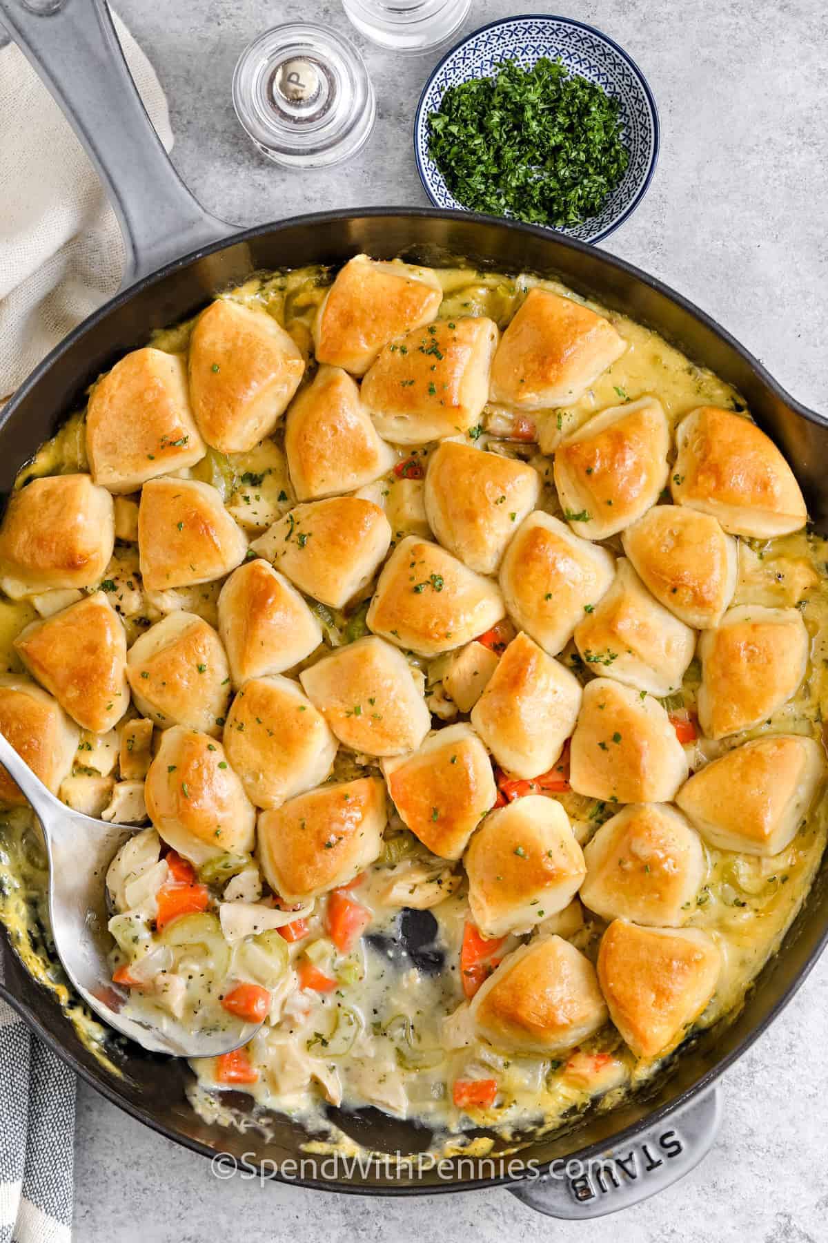 Creamy chicken and biscuits are hearty, comforting, and easy to make with a few smart shortcuts. Cooked chicken saves prep time, condensed chicken soup creates a creamy filling, and refrigerated biscuits form a fluffy golden topping without mixing dough. Carrots and celery add color, flavor, and texture to this one-pan meal. It is an easy dinner to keep in mind when leftover chicken needs a new purpose. Save this recipe for a cozy weeknight meal. #spendwithpennies chicken and biscuits in a pan with a serving spoon