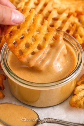 dipping waffle fries in Chick-Fil-A Sauce with spoon full beside it.