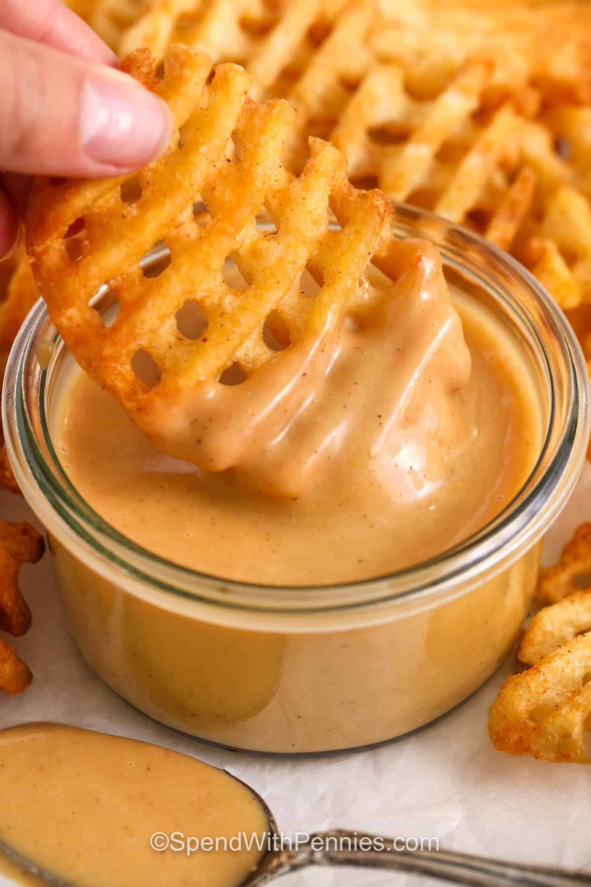 dipping waffle fries in Chick-Fil-A Sauce with spoon full beside it.