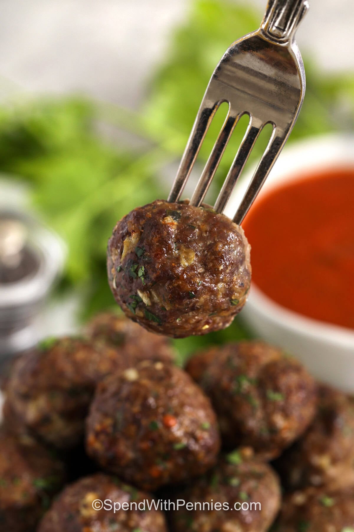 This homemade meatball recipe bakes in the oven, so there is no stovetop splatter and no need to fry in batches. The mixture uses breadcrumbs and milk for a tender texture, Parmesan for savory flavor, and parsley with Italian seasoning for a classic pasta-night taste. These baked meatballs are easy to portion, simple to freeze, and delicious with tomato sauce or spaghetti. #spendwithpennies Easy Meatball Recipe on a fork