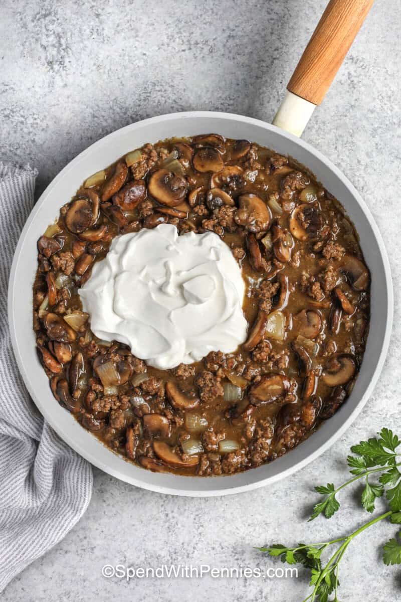 adding sour cream to Ground Beef Stroganoff mixture in pan.