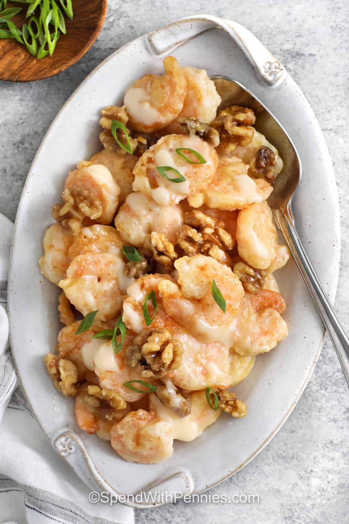 Homemade honey walnut shrimp combines tender shrimp, a light crispy coating, and crunchy candied walnuts in every bite. A simple creamy sauce made with honey, mayonnaise, sweetened condensed milk, and fresh lemon gives the shrimp the signature sweet and tangy flavor. The shrimp cook quickly in a shallow skillet, making this restaurant favorite manageable at home. Pin this shrimp recipe to try soon. #spendwithpennies juicy Honey Walnut Shrimp on a plate.