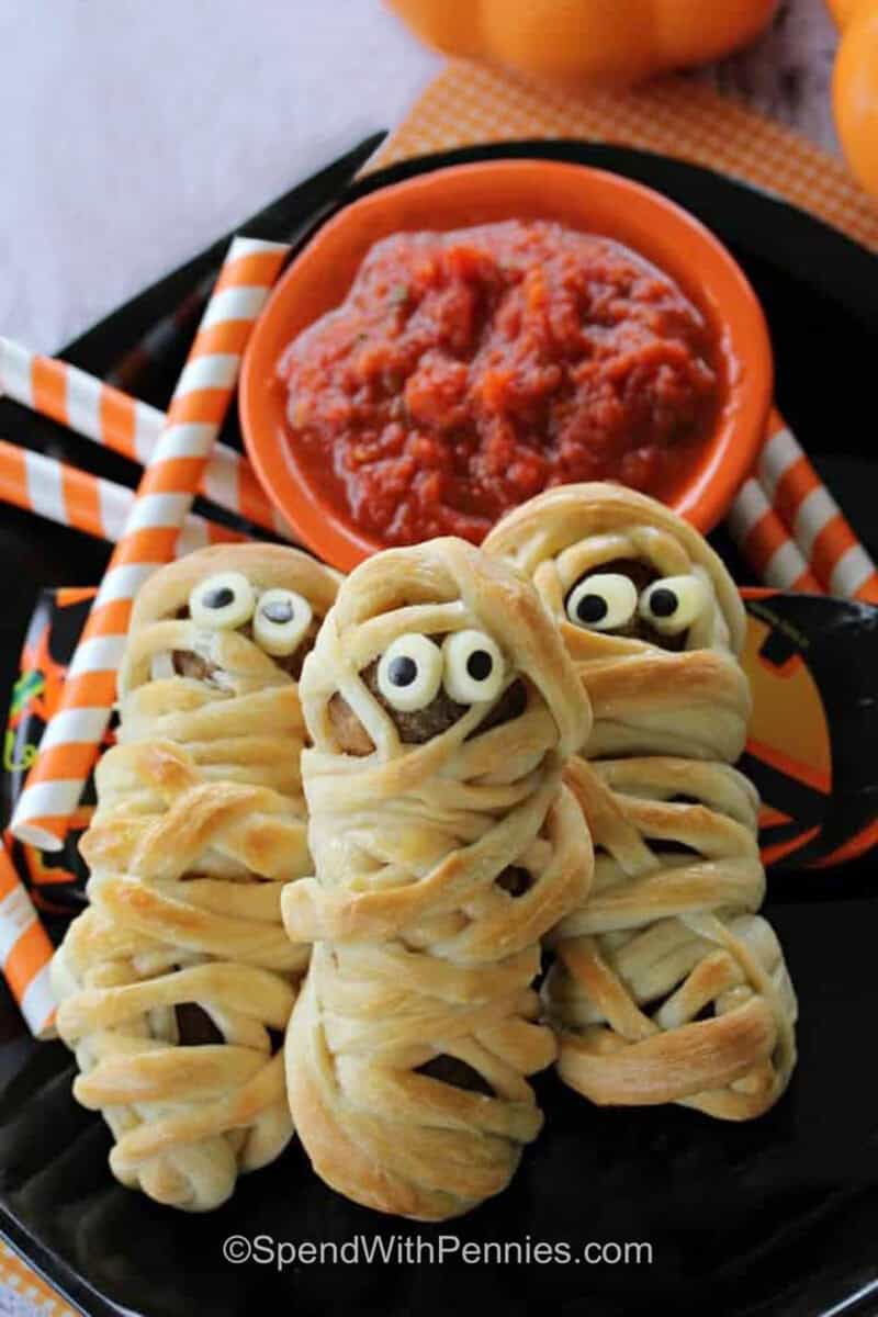 Meatball Mummies with marinara on black plate.