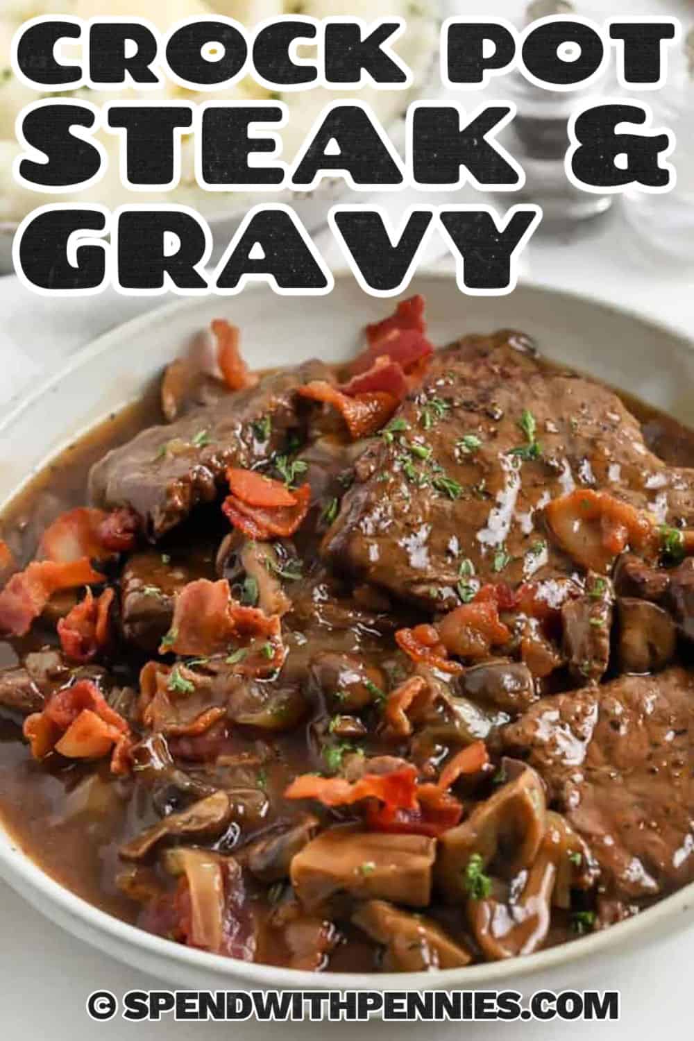 This Crock Pot steaks and gravy recipe makes affordable beef taste incredibly tender and flavorful. Browning the steaks before slow cooking creates a rich gravy with deep savory flavor. It's an easy make-ahead dinner that's perfect for busy weekdays, Sunday supper, or freezer meal planning. Pin it now so it's ready for your next comforting meal. #spendwithpennies savory Crock Pot Steak & Gravy on a plate with a title.