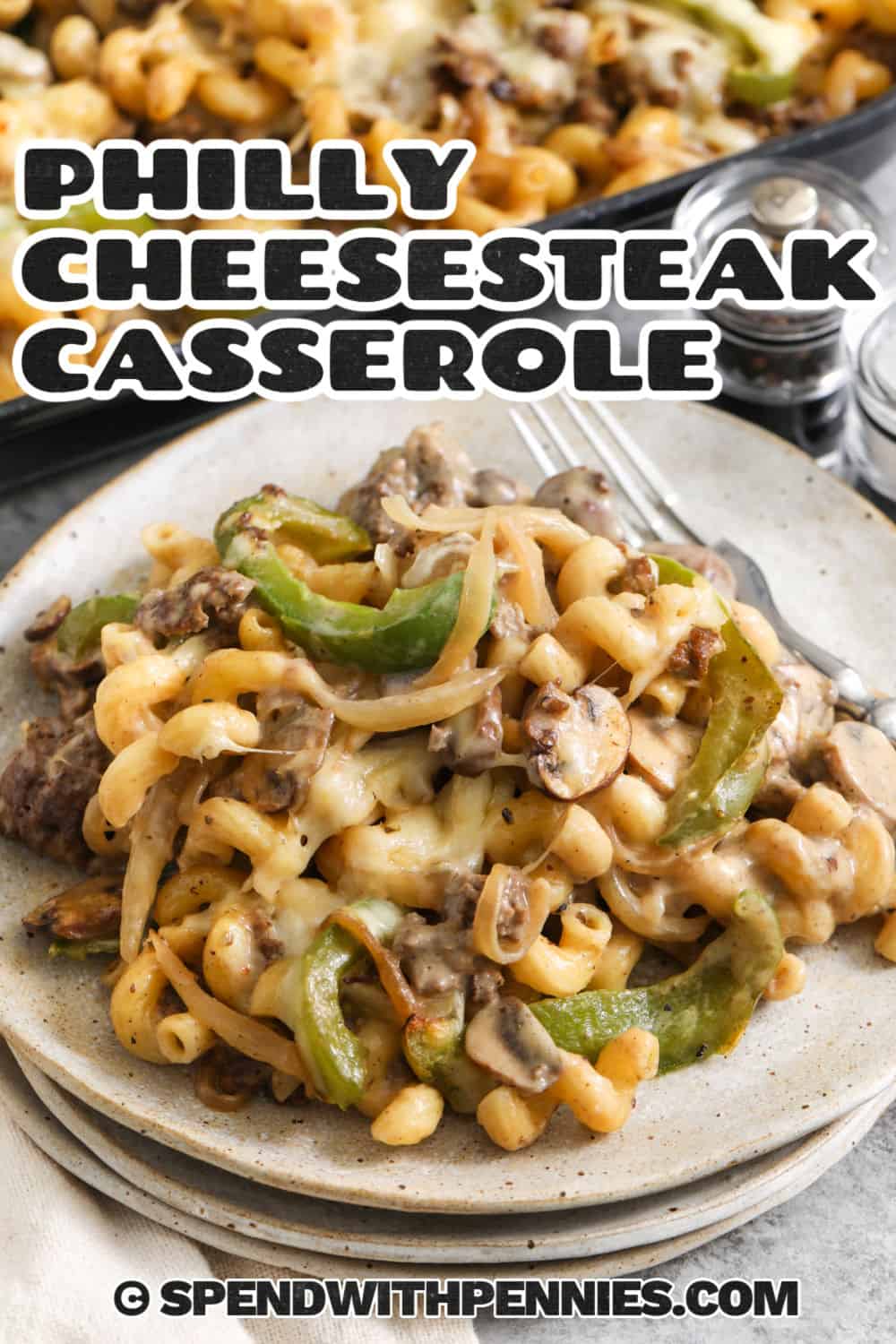 Philly cheesesteak casserole is an easy comfort-food dinner packed with seasoned beef, sautéed green peppers, mushrooms, onions, and tender pasta. A homemade sauce with beef broth, half-and-half, Swiss, and pepper jack coats every bite before the casserole is baked until hot and bubbly. Ground beef keeps this version practical while still delivering plenty of savory flavor. Save this cheesy casserole for a busy weeknight. #spendwithpennies plate of Philly Cheesesteak Casserole with dish full in the background with a title.