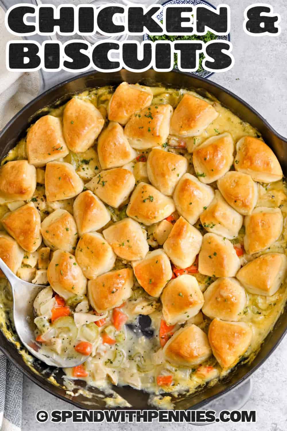 This easy chicken and biscuits recipe is pure comfort food with tender cooked chicken, carrots, and celery tucked into a creamy, savory sauce. Refrigerated biscuits are cut into pieces and baked right on top until fluffy inside and beautifully golden around the edges. Using cooked or rotisserie chicken keeps prep quick, and the entire dinner comes together in one oven-safe skillet. Save this easy recipe for your next cozy weeknight dinner. #spendwithpennies chicken and biscuits in an oven safe skillet with writing.