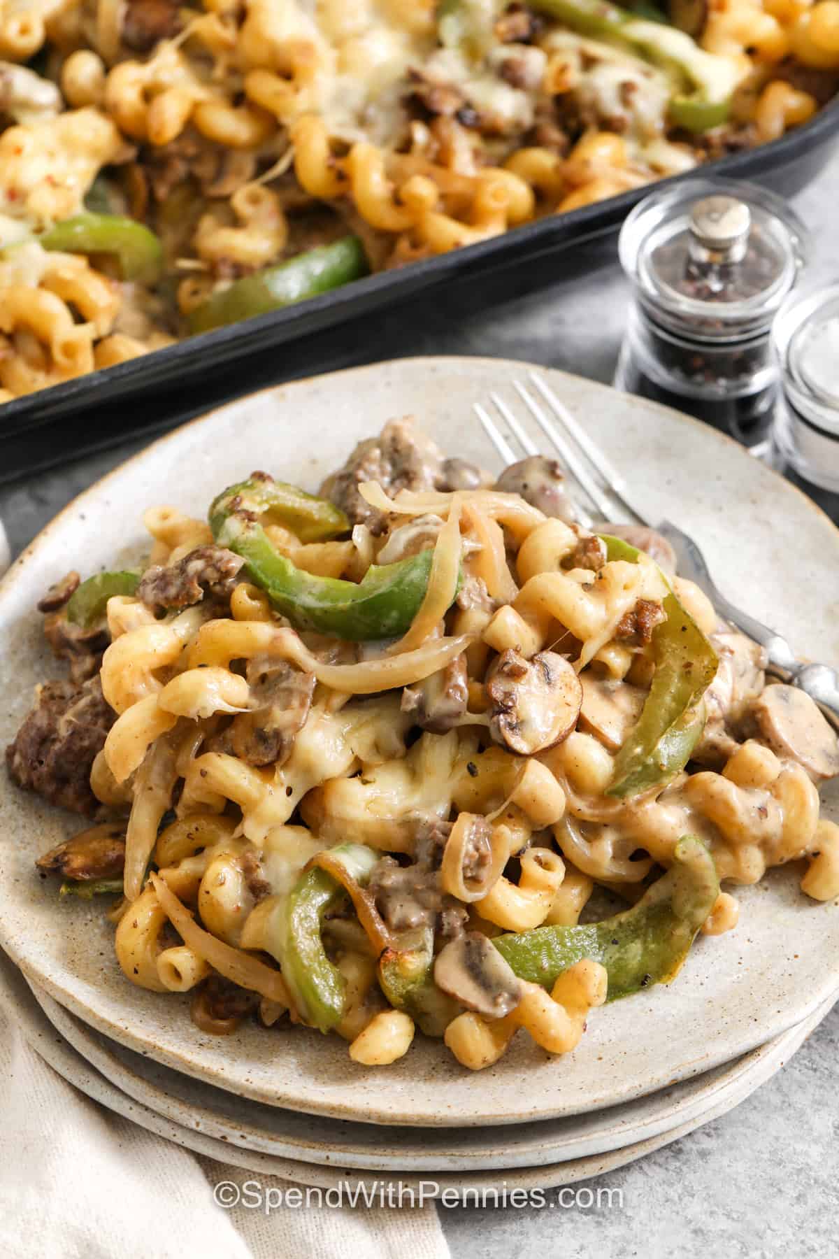 This Philly cheesesteak casserole is an easy way to make six hearty servings with one pound of ground beef. Seasoned beef, green pepper, mushrooms, and onions are mixed with cavatappi and a smooth homemade cheese sauce, then topped with pepper jack and baked until bubbly. The combination is creamy, savory, and satisfying without requiring steak. Pin this practical pasta casserole for family dinners and meal planning. #spendwithpennies plated Philly Cheesesteak Casserole.