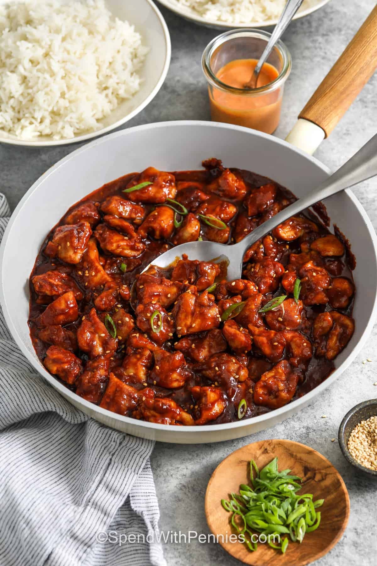 Honey gochujang chicken has tender bites of chicken coated in a sweet, spicy, and savory sauce that comes together right in the skillet. Fresh ginger and garlic add plenty of flavor, while rice vinegar balances the honey and rich fermented chili paste. Add rice, broccoli, or a crunchy slaw on the side for an easy meal that works just as well for weeknight dinner as it does for meal prep. Save this flavorful chicken recipe. #spendwithpennies pan of Gochujang Chicken with a spoon.