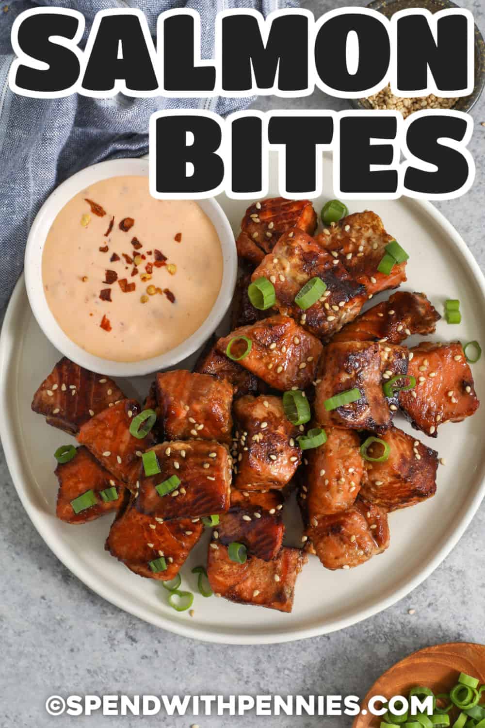 Honey garlic salmon bites are an easy way to turn a salmon fillet into a fast, flavorful meal. A simple honey and soy sauce marinade coats every piece with sweet, savory flavor before the salmon is pan seared until golden at the edges. Add rice and crisp vegetables for a satisfying bowl, or serve the bites with spicy mayo as an appetizer. Save this easy salmon bites recipe for your next busy weeknight. #spendwithpennies Top view of Salmon Bites on a plate with dipping sauce and writing.