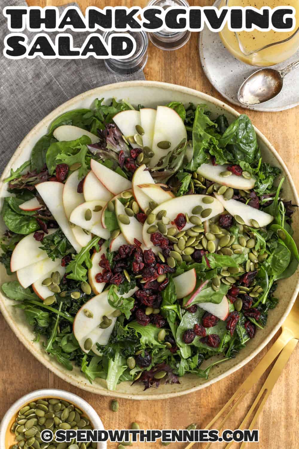 This kale apple Thanksgiving salad makes a colorful addition to Thanksgiving dinner without taking up precious oven or stovetop space. Thinly sliced kale is massaged with apple cider vinaigrette until tender, then combined with fresh mixed greens, crisp apple, dried cranberries, and pumpkin seeds. The result is sweet, tangy, crunchy, and fresh enough to balance richer holiday dishes. Pin this Thanksgiving salad recipe for an easy holiday side. #spendwithpennies Top view of Thanksgiving salad with writing.