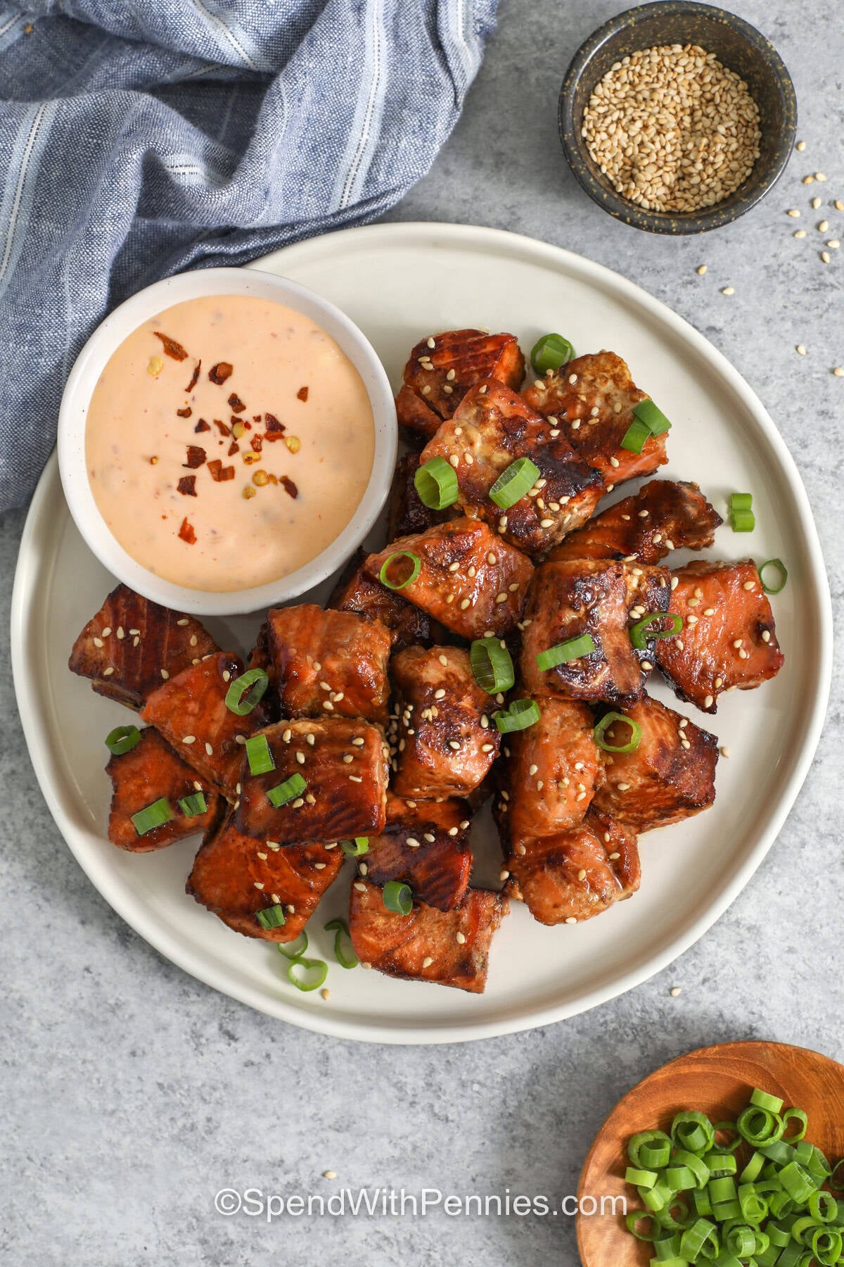 Crispy salmon bites have lightly caramelized edges, tender flaky centers, and a simple honey garlic flavor that works for lunch or dinner. Cut the salmon into even pieces, give it a short soak in the soy and honey marinade, then sear it in a hot skillet until golden. Pair the bites with rice and vegetables or a creamy spicy mayo dip. Save this salmon bites recipe when you need an easy seafood meal with minimal prep. #spendwithpennies Salmon Bites top view on a white plate with dip.
