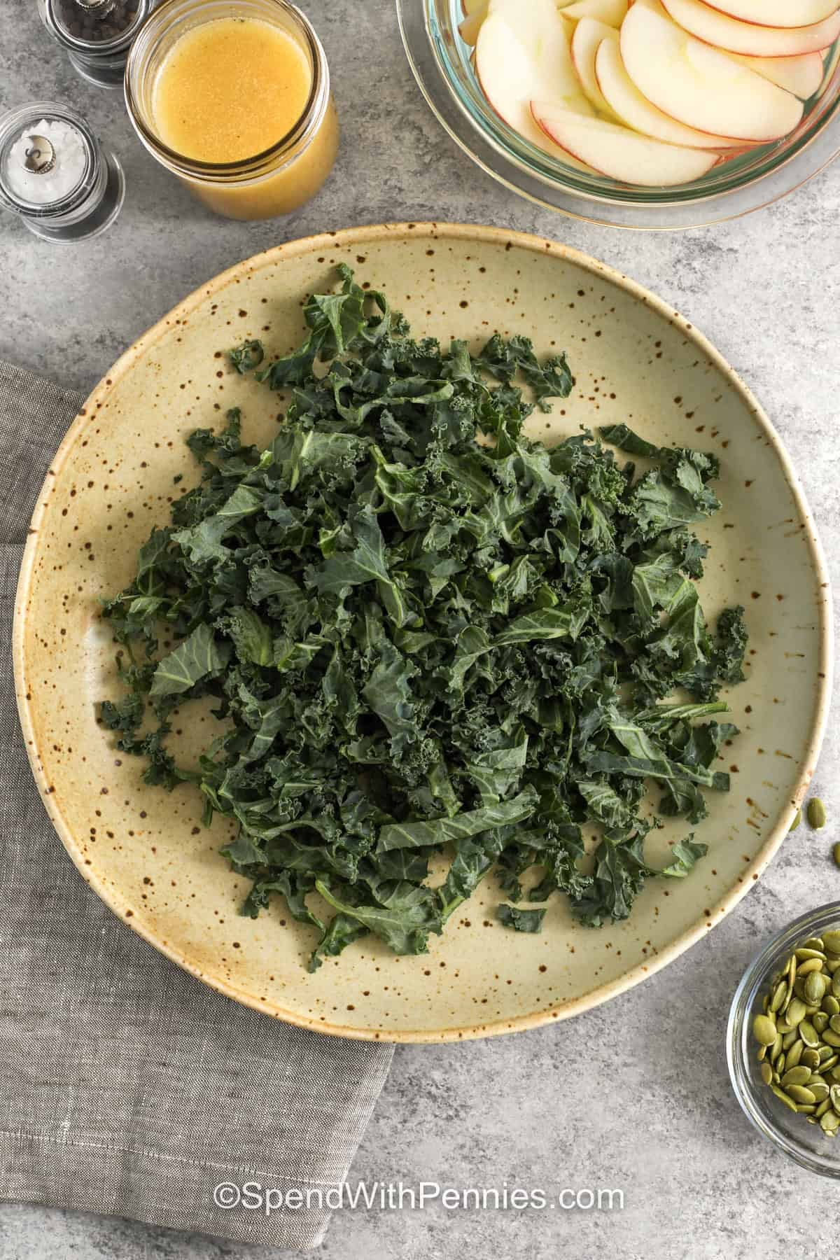This fall green Thanksgiving salad combines tender kale and mixed greens with crisp apples, sweet-tart cranberries, and crunchy pumpkin seeds. A quick homemade apple cider vinaigrette adds honeyed sweetness, Dijon tang, and plenty of bright flavor without overwhelming the fresh ingredients. Prepare the dressing and apples ahead, then assemble near serving time for the best texture. Save this easy salad for Thanksgiving or any fall dinner. #spendwithpennies Chopped kale for Thanksgiving Salad.